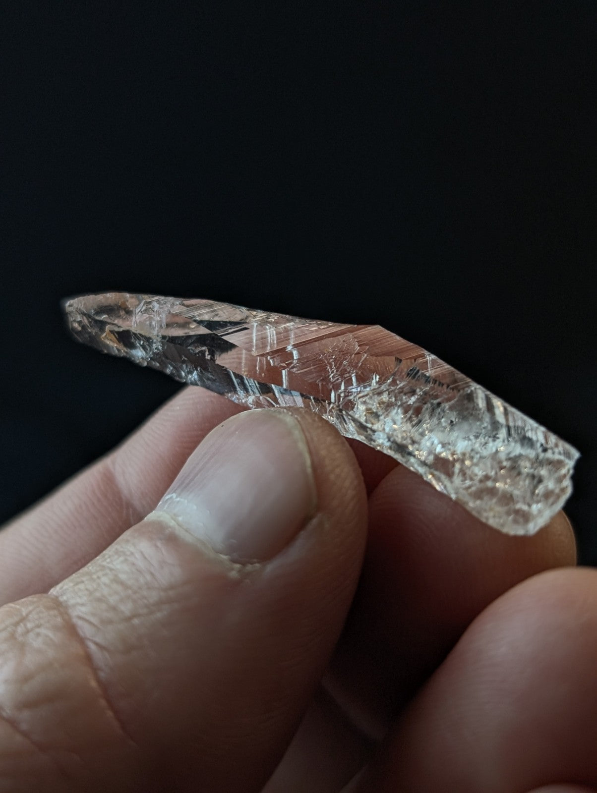 A translucent, faceted crystal with a subtle pinkish hue and intricate internal fractures.