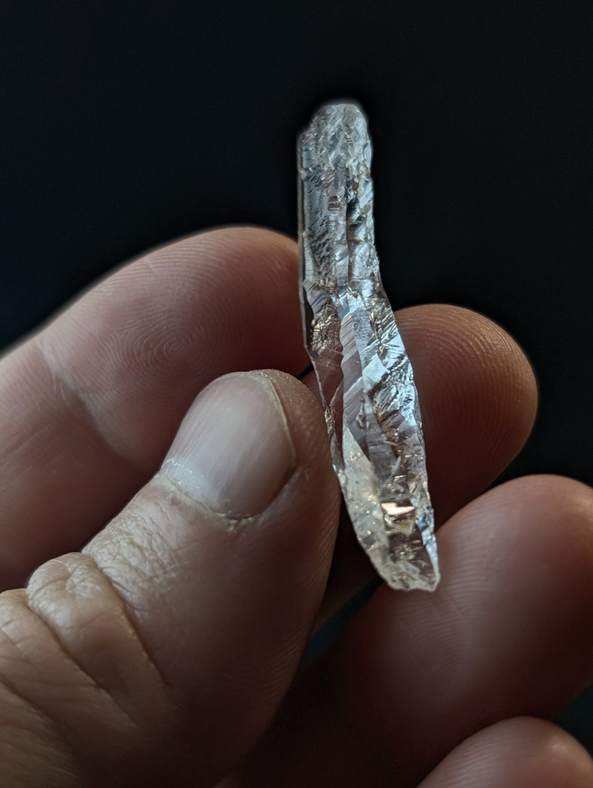 A translucent, clear quartz crystal with natural striations and facets held gently in a hand.