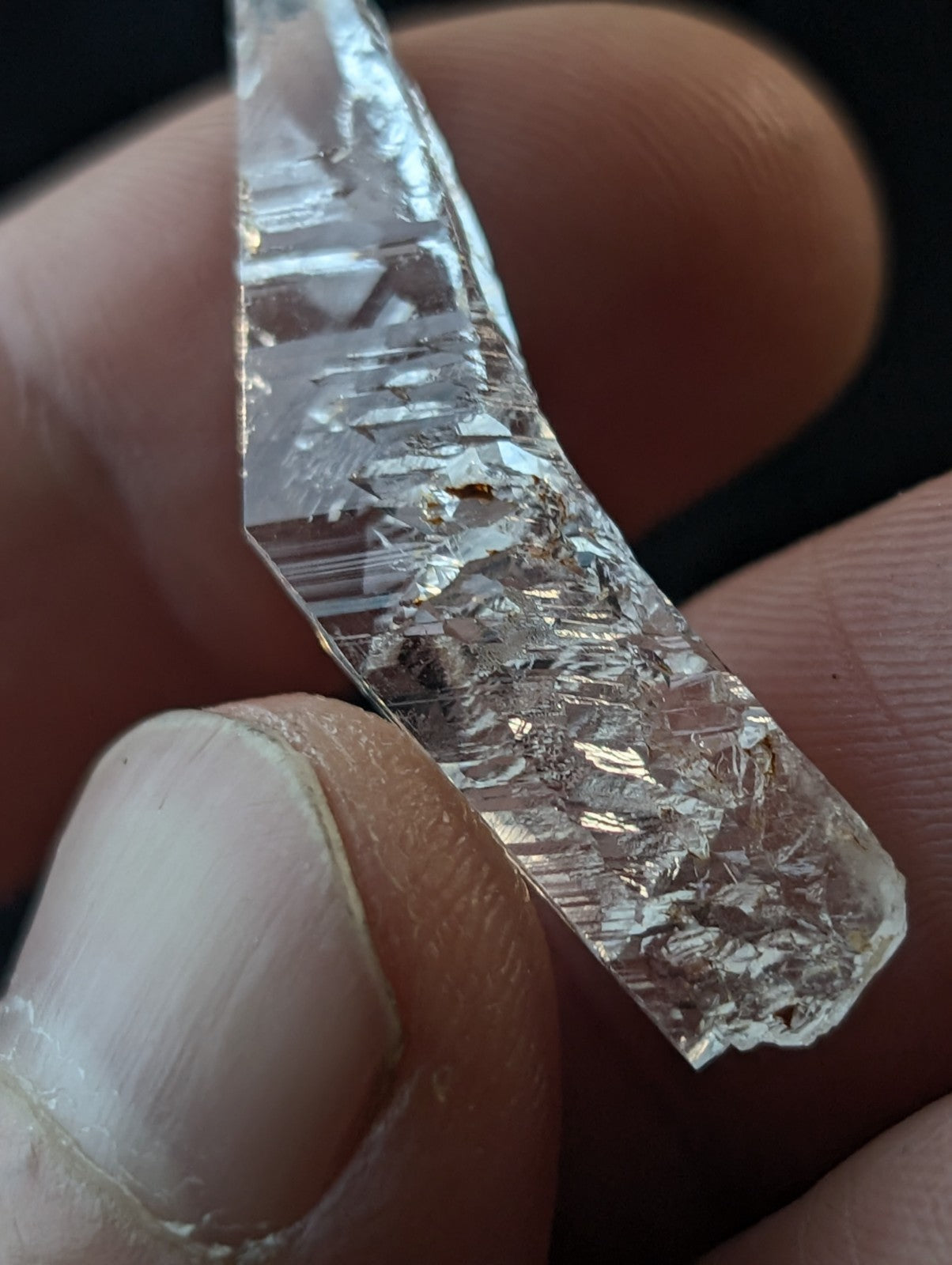 A clear, faceted crystal with visible internal striations and a rough, jagged edge.
