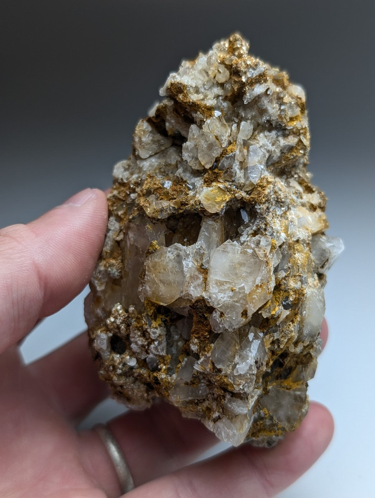 A hand holds a very unique translucent quartz cluster with golden yellow cookeite veins from Saline County Arkansas
