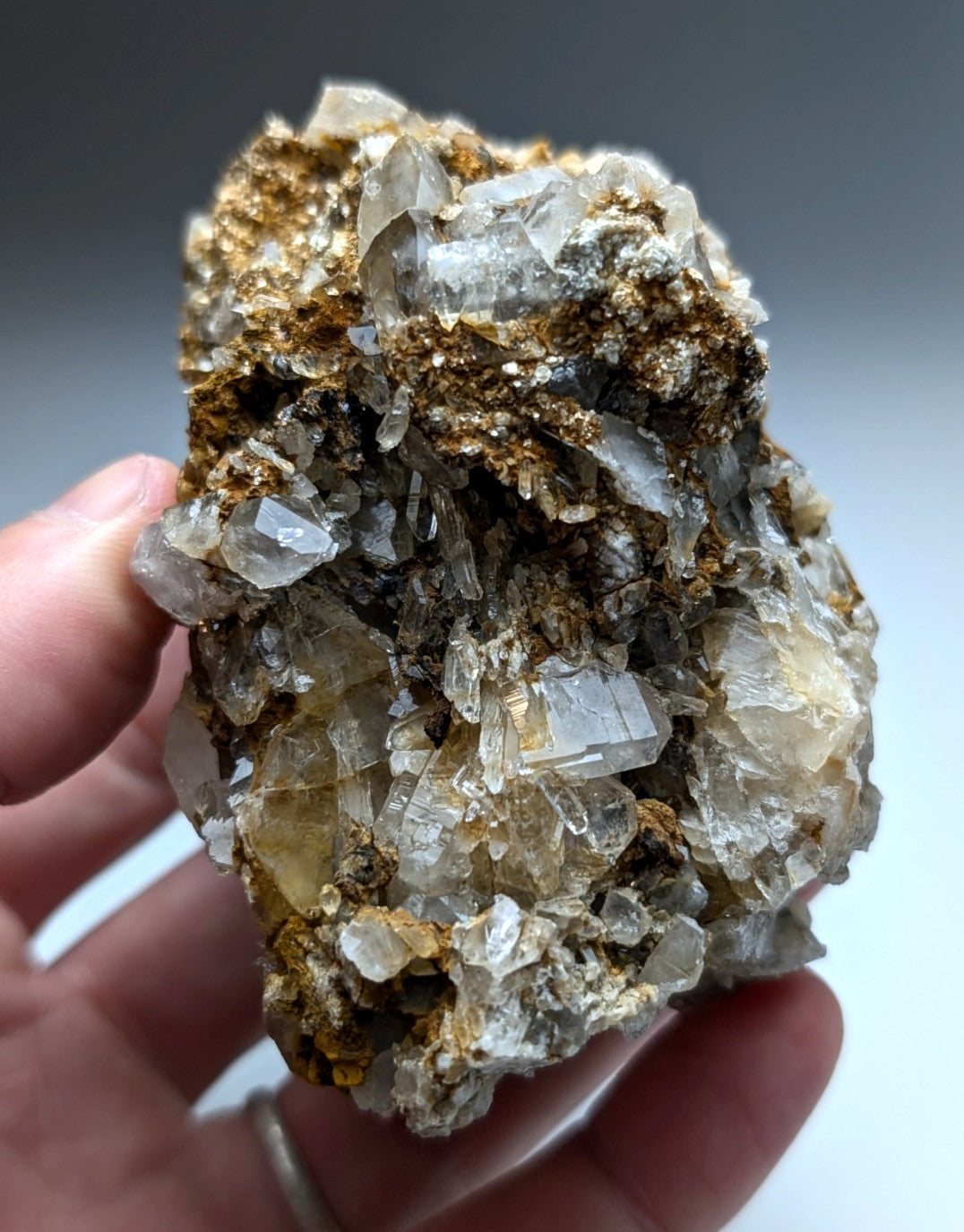 A hand holds a very unique quartz cookeite conglomerate cluster with translucent crystals and golden-brown mineral matrix
