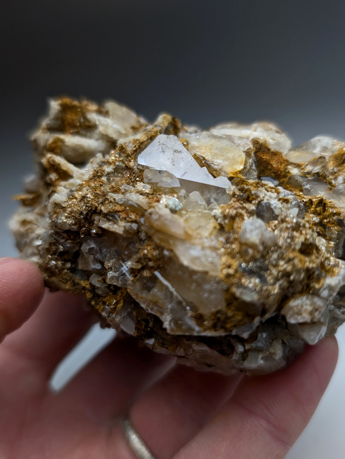A hand holds a very unique translucent quartz conglomerate cluster with golden cookeite inclusions from arkansas
