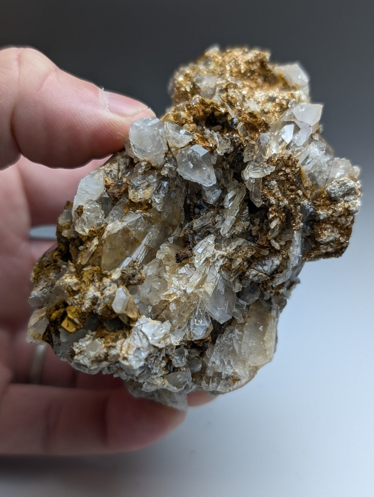 A hand holds a very unique quartz and cookeite conglomerate with translucent crystals and golden-yellow metallic inclusions