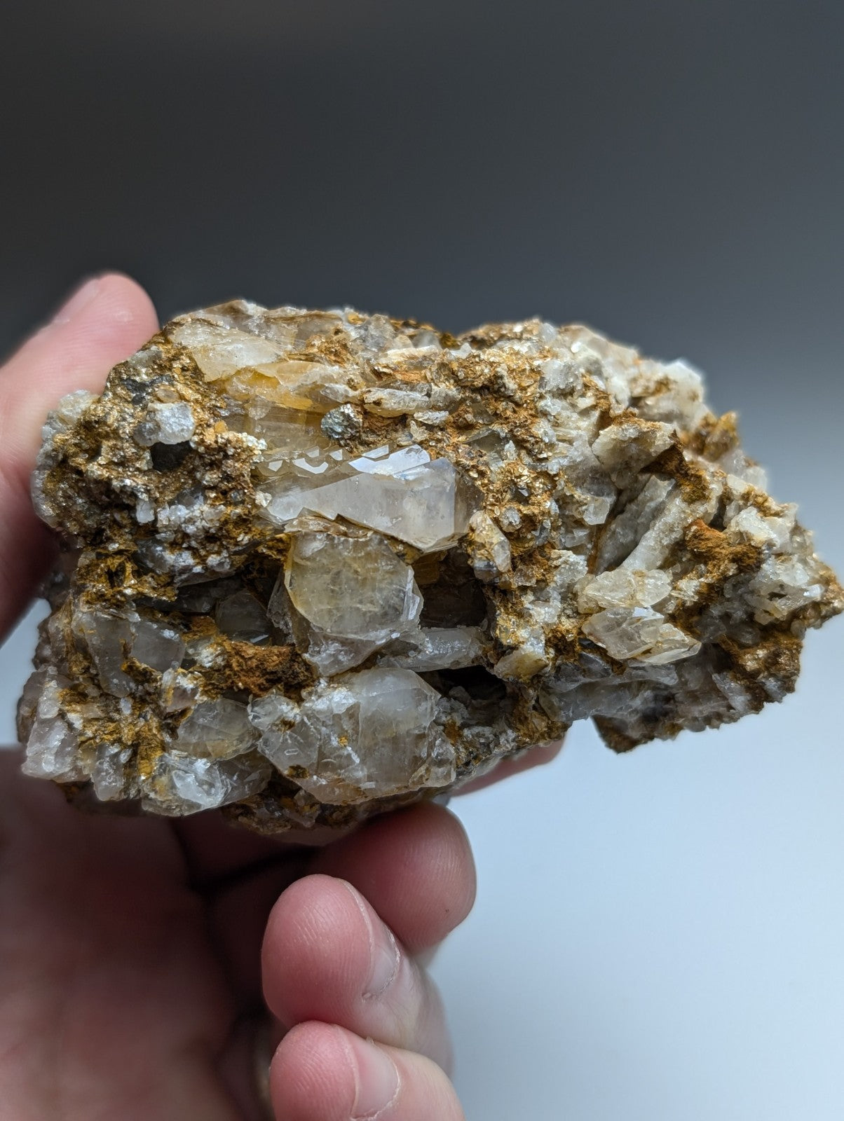 A hand holds a very unique quartz and cookeite conglomerate with translucent crystals and golden-brown mineral matrix