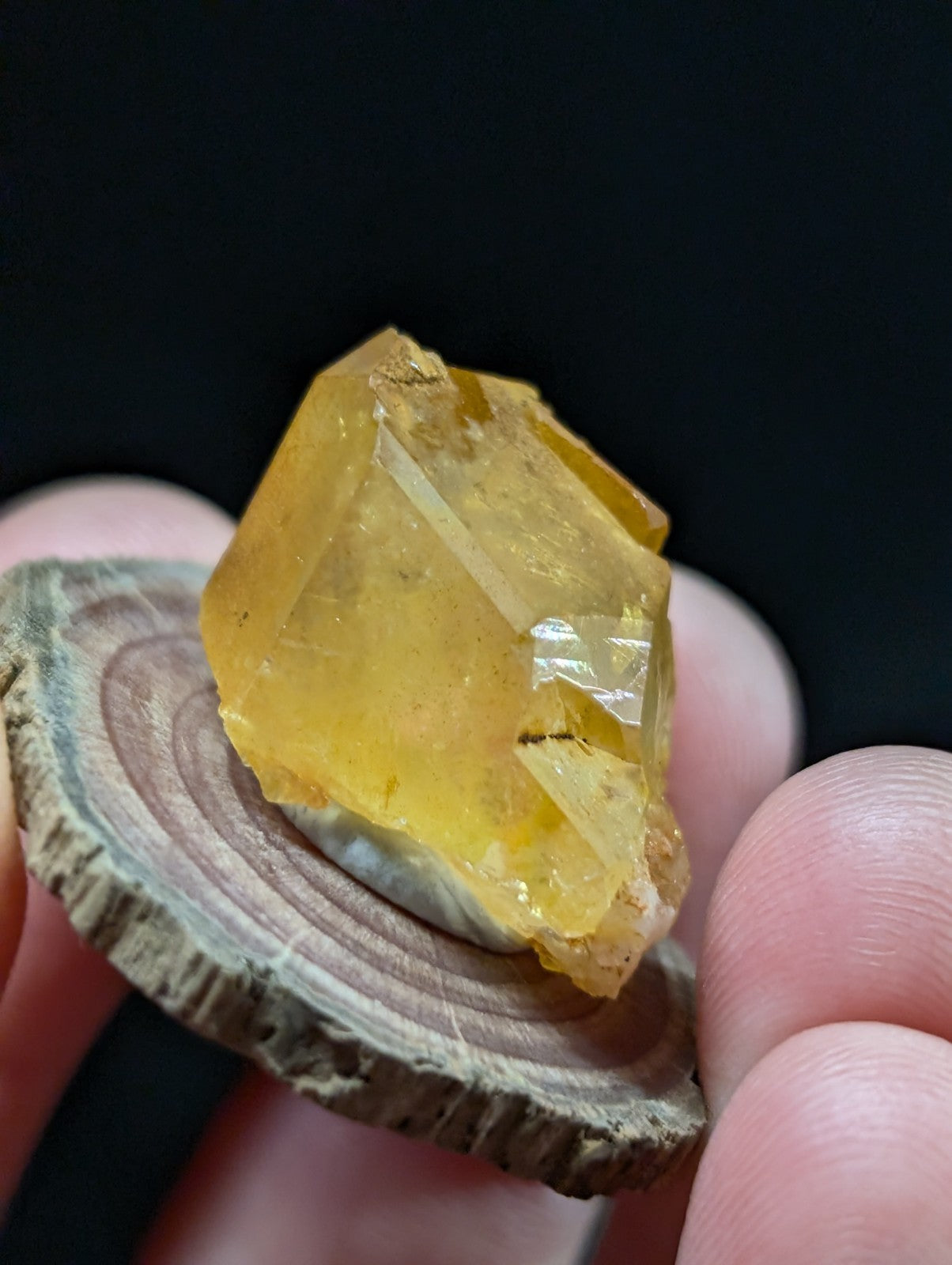 A translucent yellow crystal with sharp, angular facets rests on a circular wooden slice.