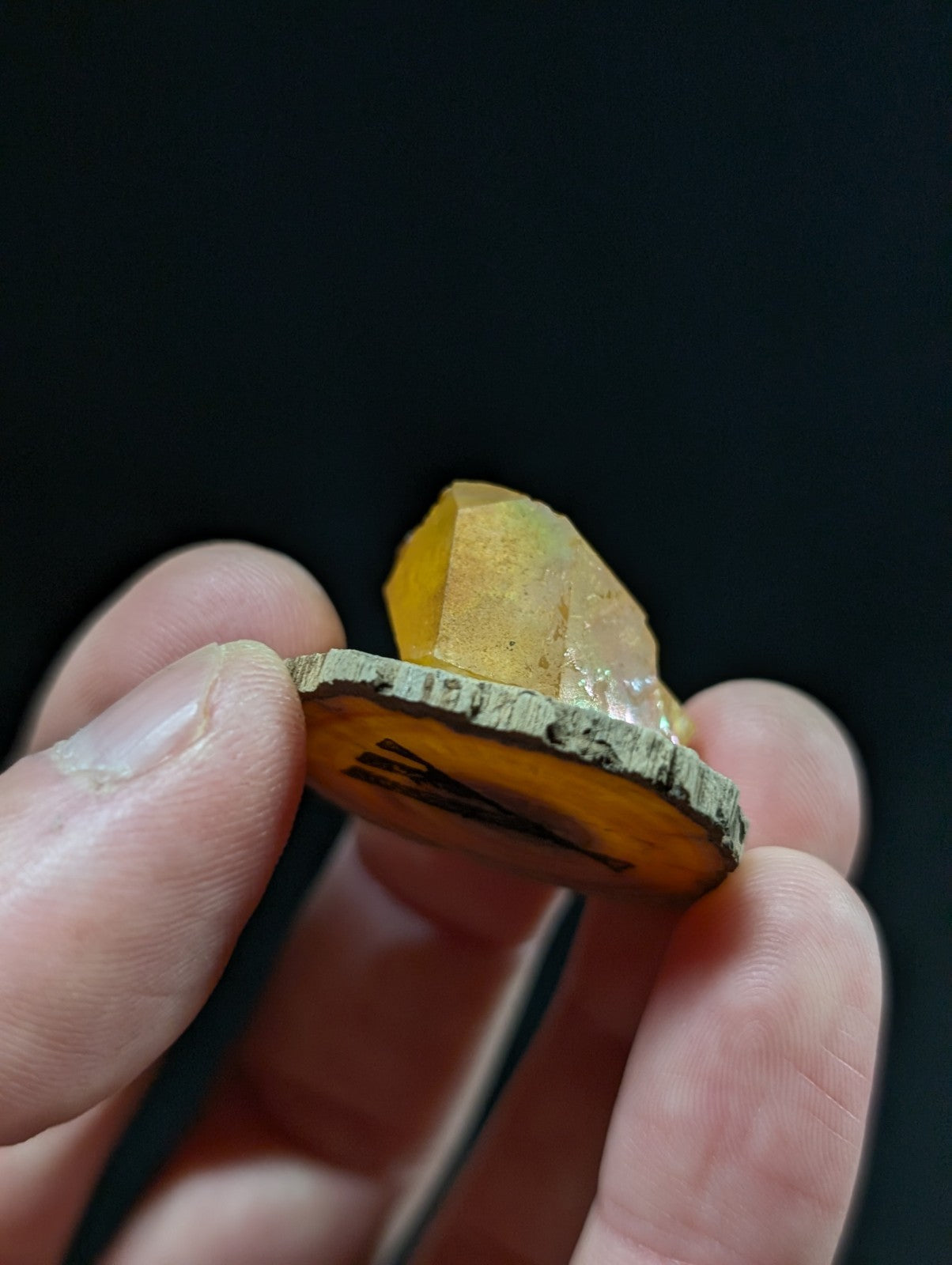 A polished amber-colored crystal with a rough, natural wood base and engraved markings.