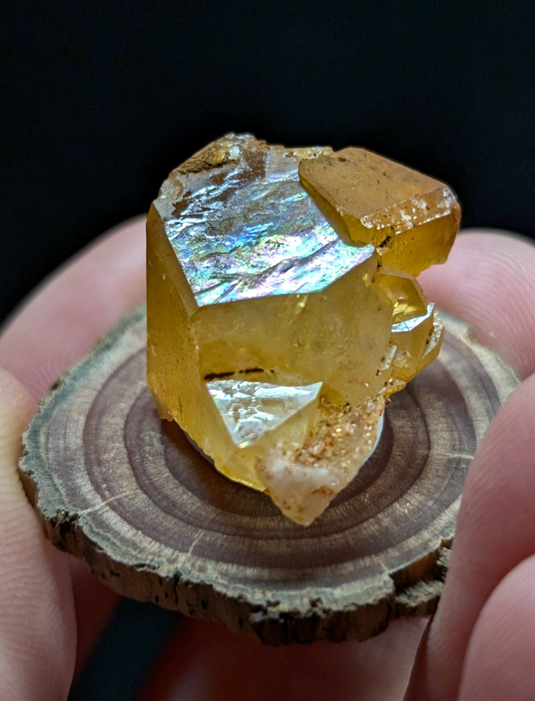 A translucent golden-yellow mineral crystal with iridescent, rainbow-hued facets and a rough, earthy base.