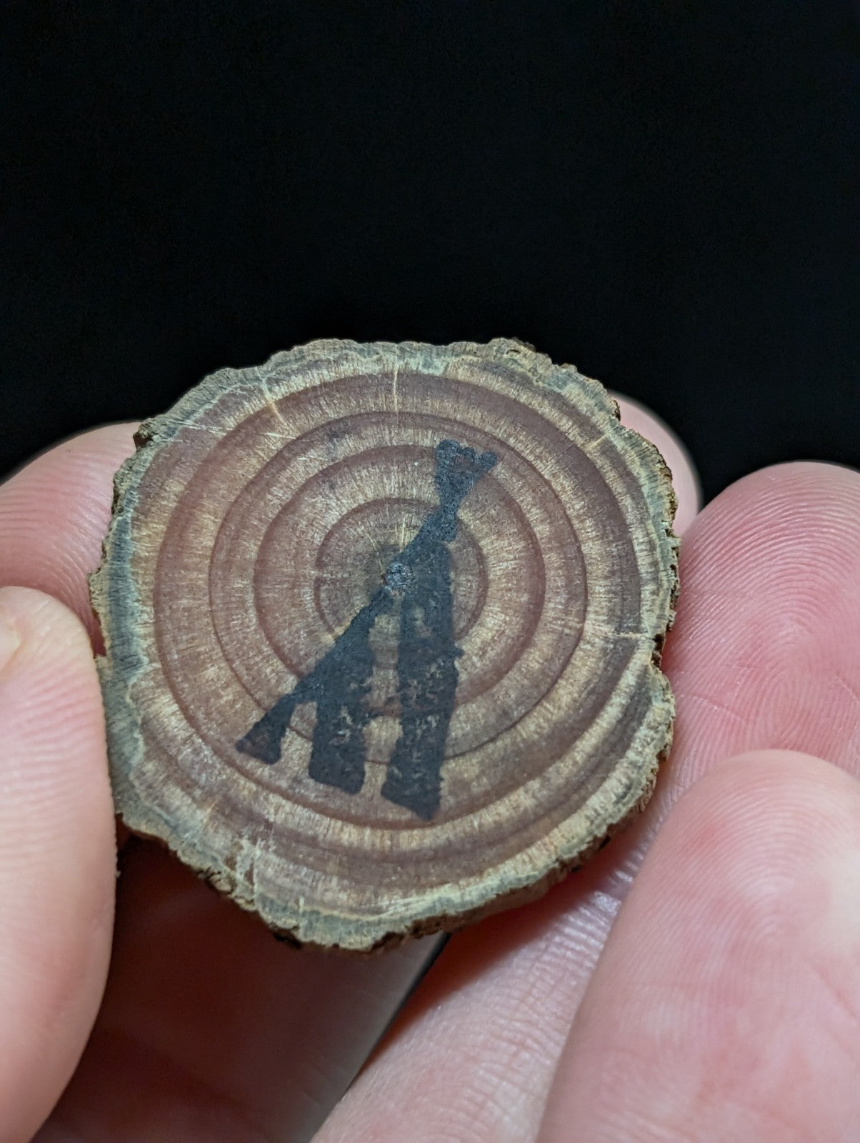 A circular wooden slice with visible growth rings, featuring a black silhouette of an axe engraved or painted onto its surface.