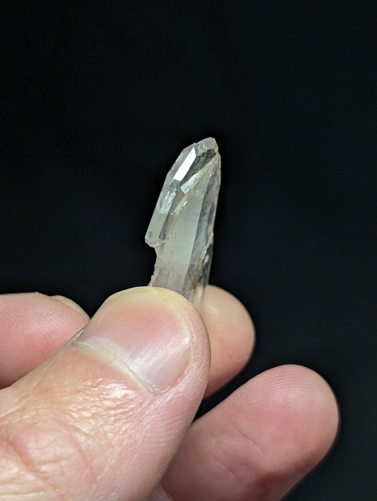 A translucent, clear quartz crystal with a pointed tip and faceted surface.