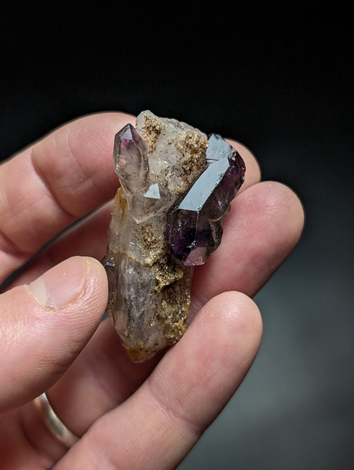 A hand holds a cluster of amethyst and clear quartz crystals, showcasing their natural facets and earthy matrix.