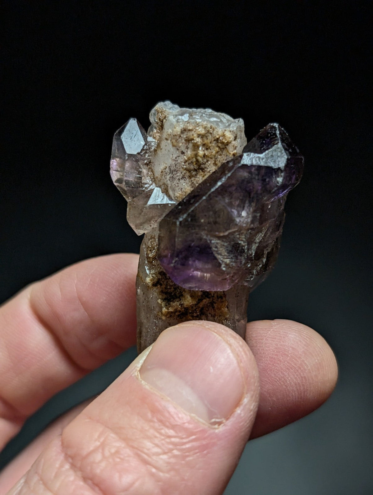 A cluster of translucent amethyst and clear quartz crystals, showcasing natural facets with earthy matrix material.