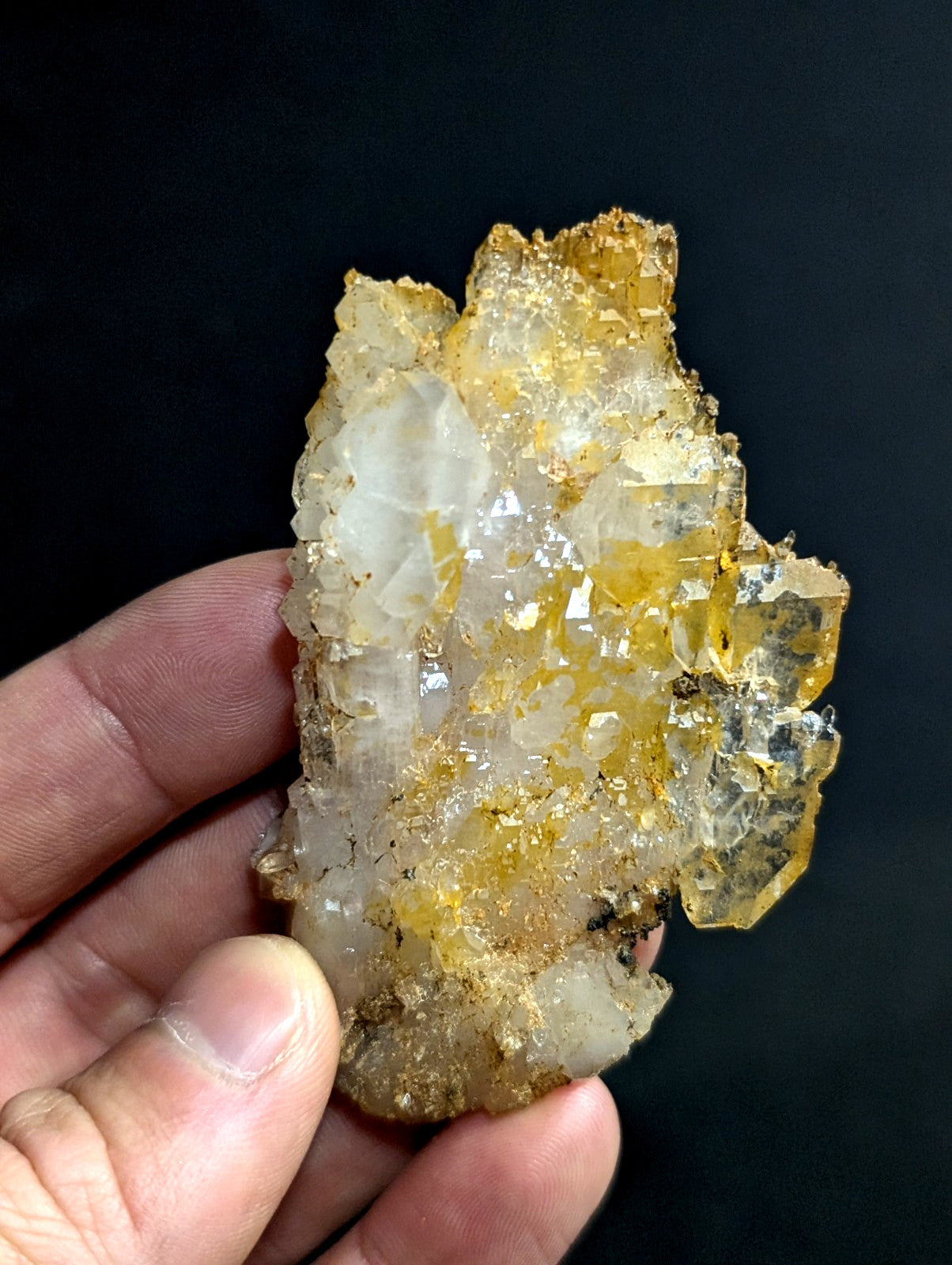A translucent yellow and white crystal cluster with jagged, faceted surfaces held in a hand.