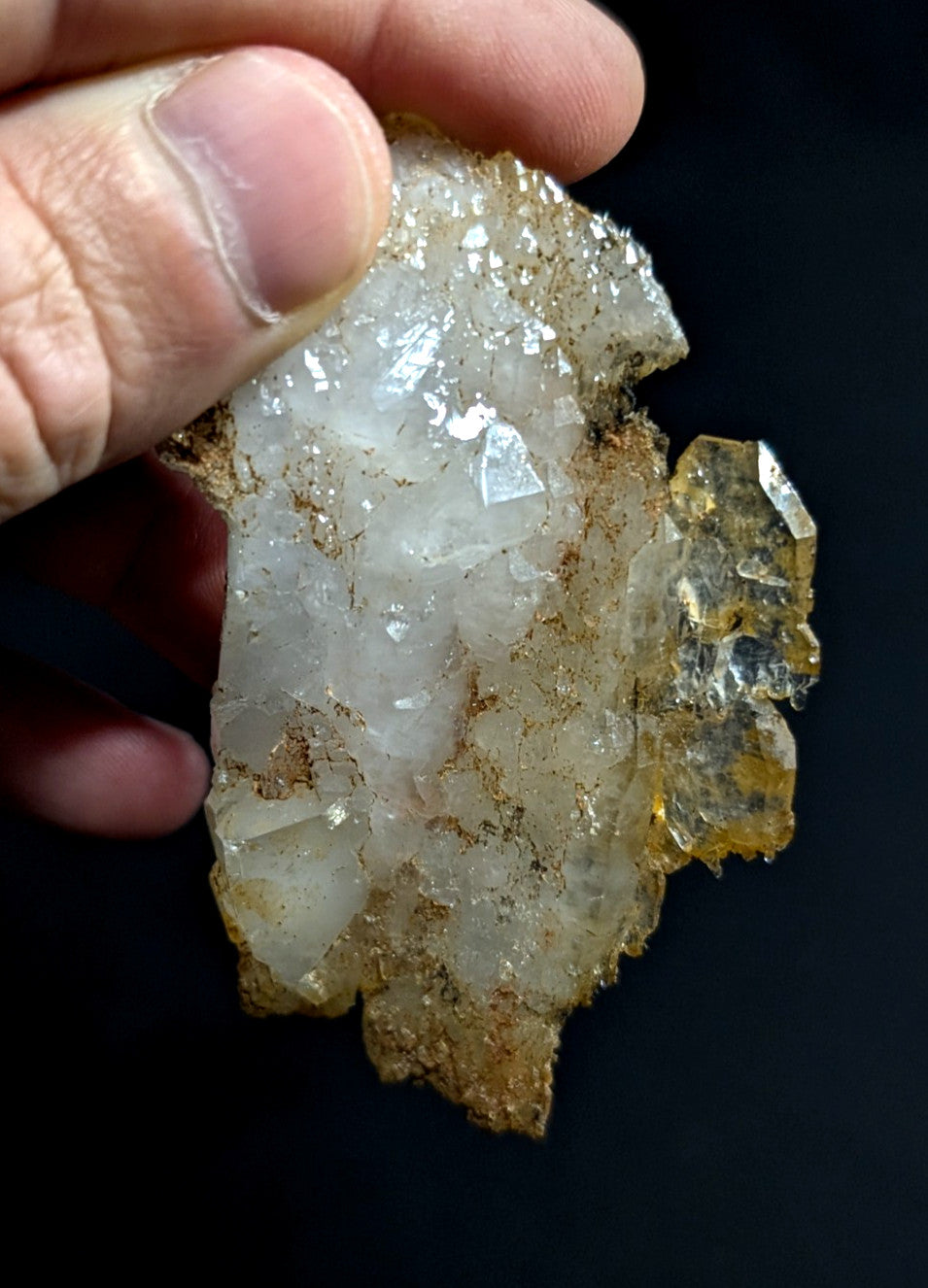 A translucent white quartz crystal cluster with golden-brown mineral matrix, held in hand against a dark background.