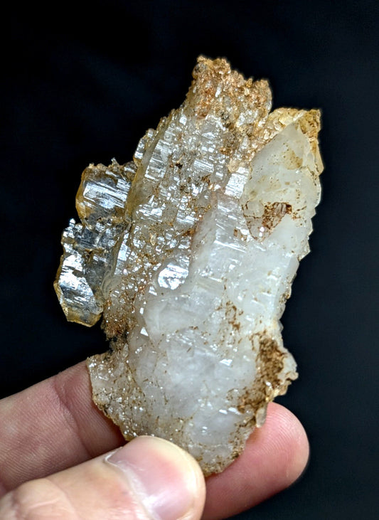 A translucent white and golden mineral specimen with crystalline facets, held gently in a hand against a dark background.