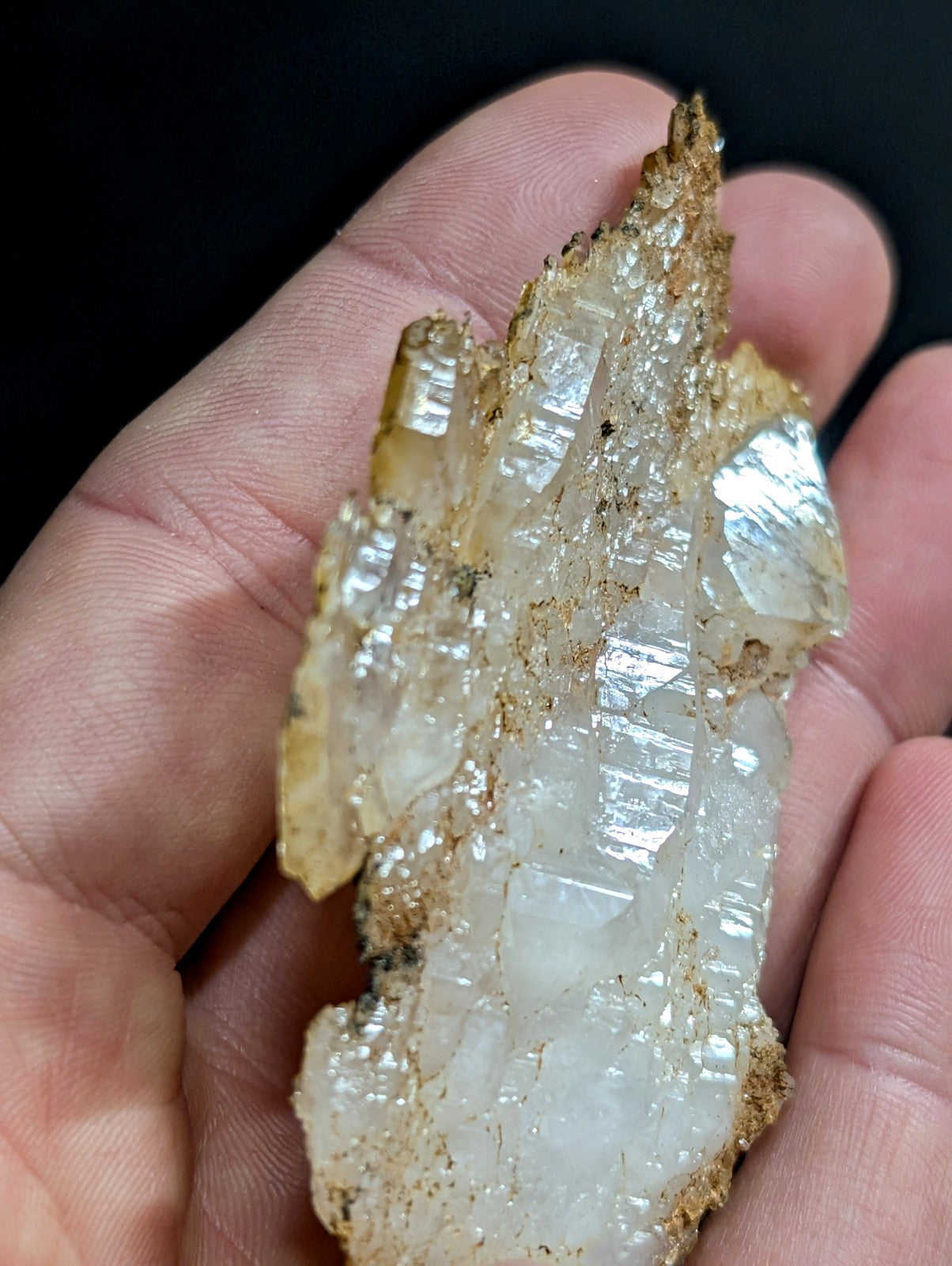 A translucent white quartz crystal cluster with golden-brown mineral matrix, held in a hand.