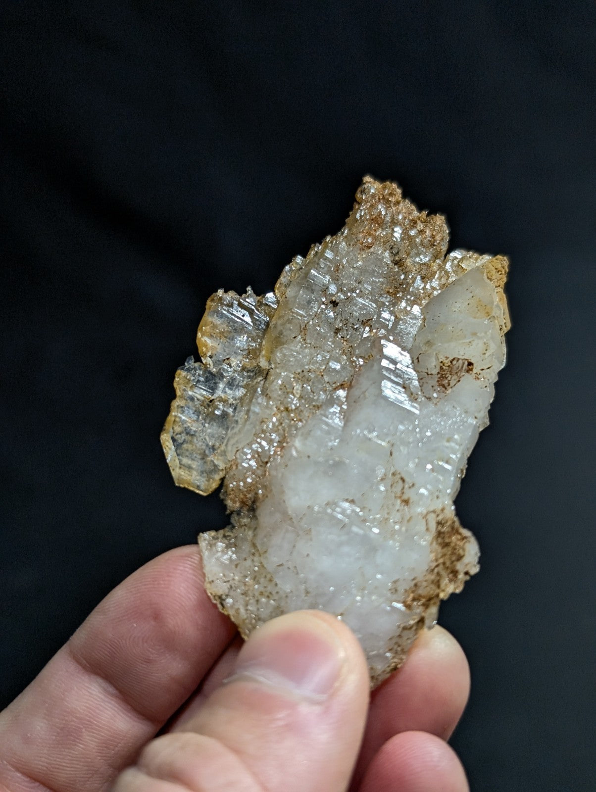 A translucent white quartz crystal cluster with golden-brown mineral inclusions, held gently between fingers.