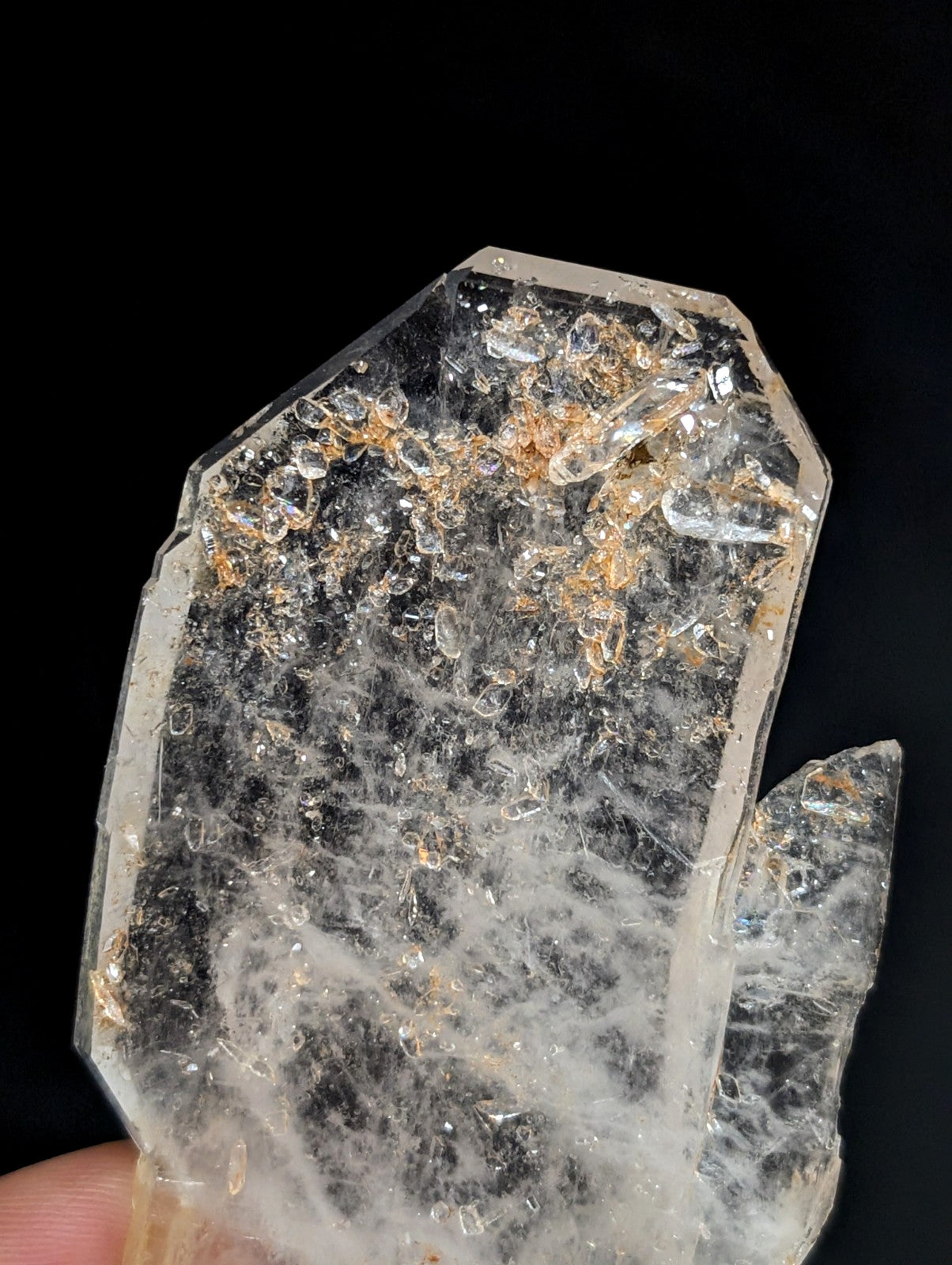 A translucent, clear quartz crystal with a rough, faceted surface and embedded golden-brown inclusions.
