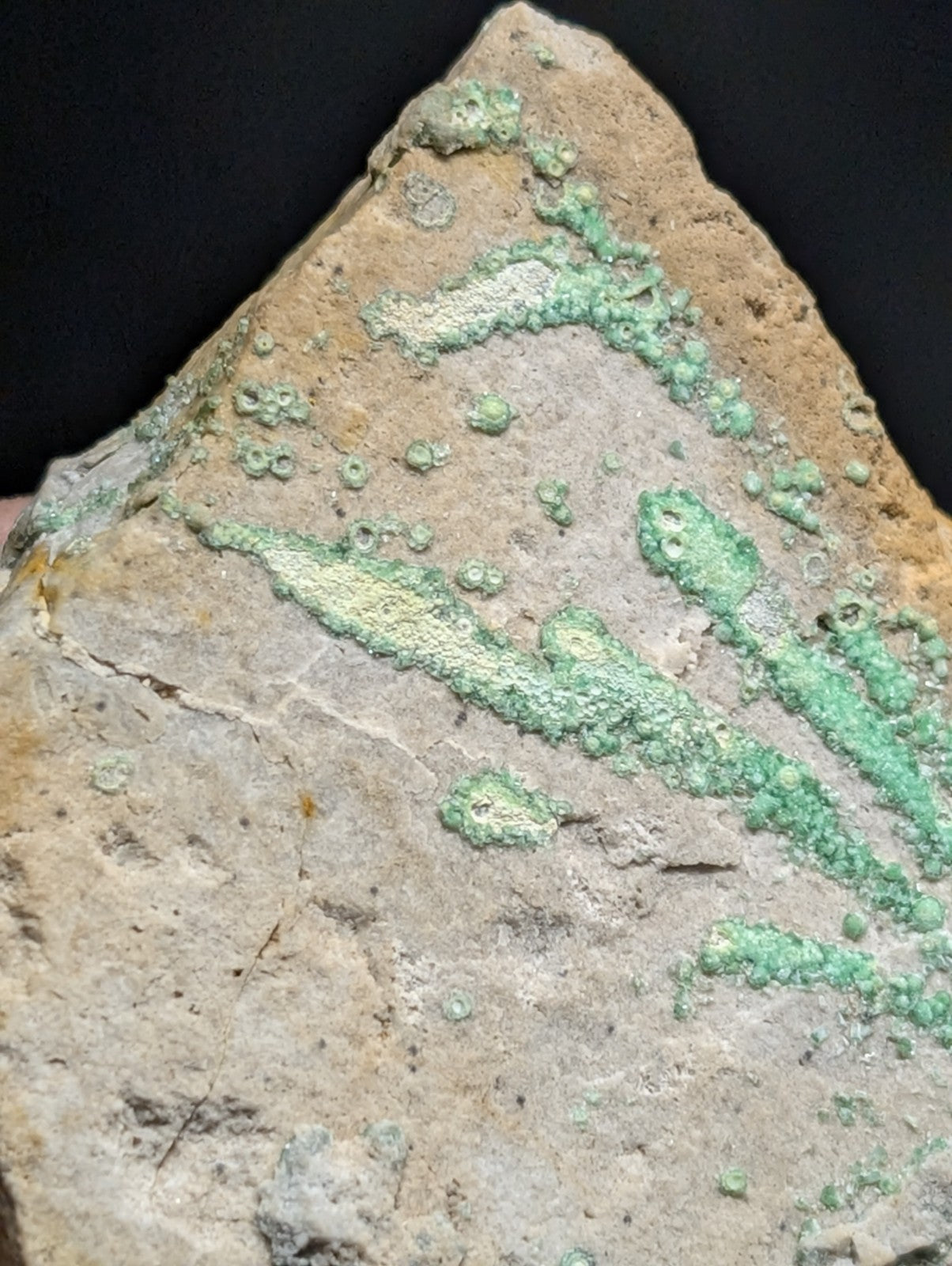 A weathered, triangular ceramic shard with patches of green patina and a rough, textured surface.