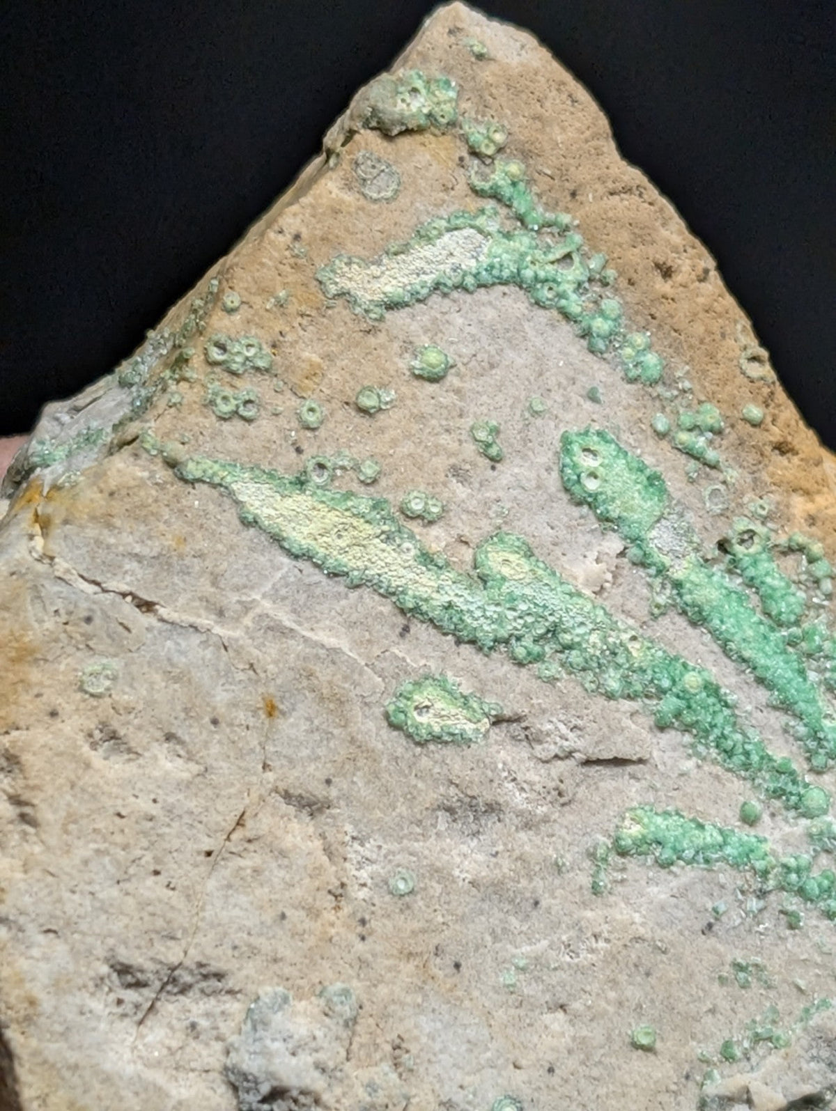 A weathered, triangular ceramic shard with patches of green patina and a rough, textured surface.