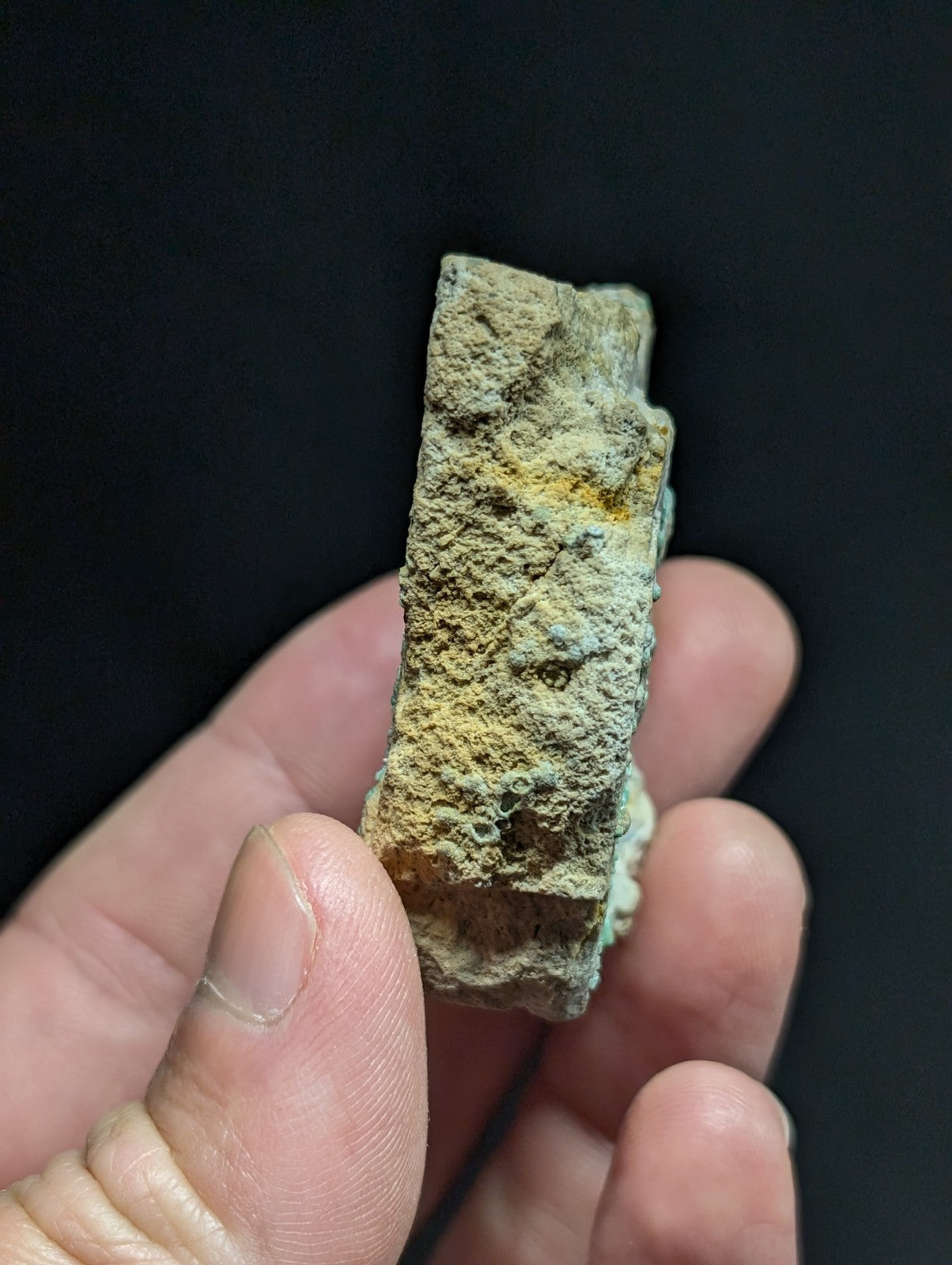 A weathered, rectangular ancient artifact with a rough, textured surface covered in patches of green and yellow patina.