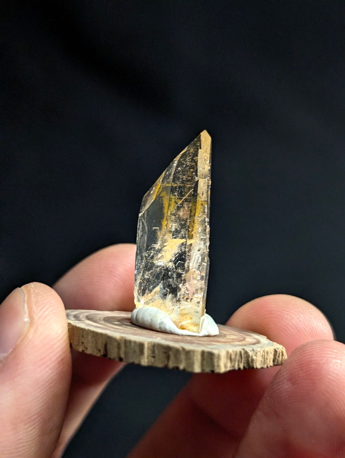 A translucent golden-yellow crystal with natural inclusions, mounted on a circular wooden base.