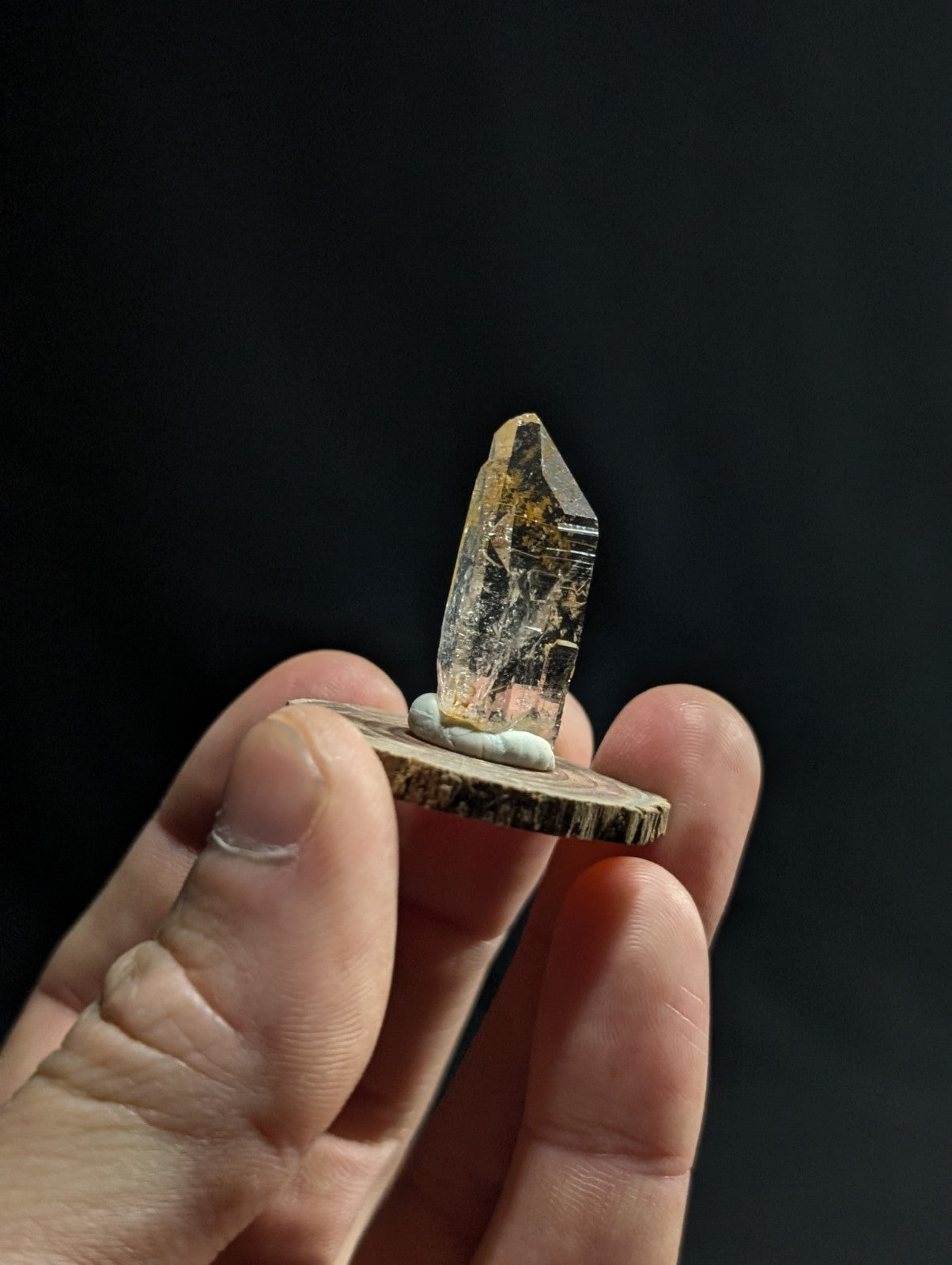 A translucent, amber-hued quartz crystal with a pointed tip stands upright on a rustic wooden base.