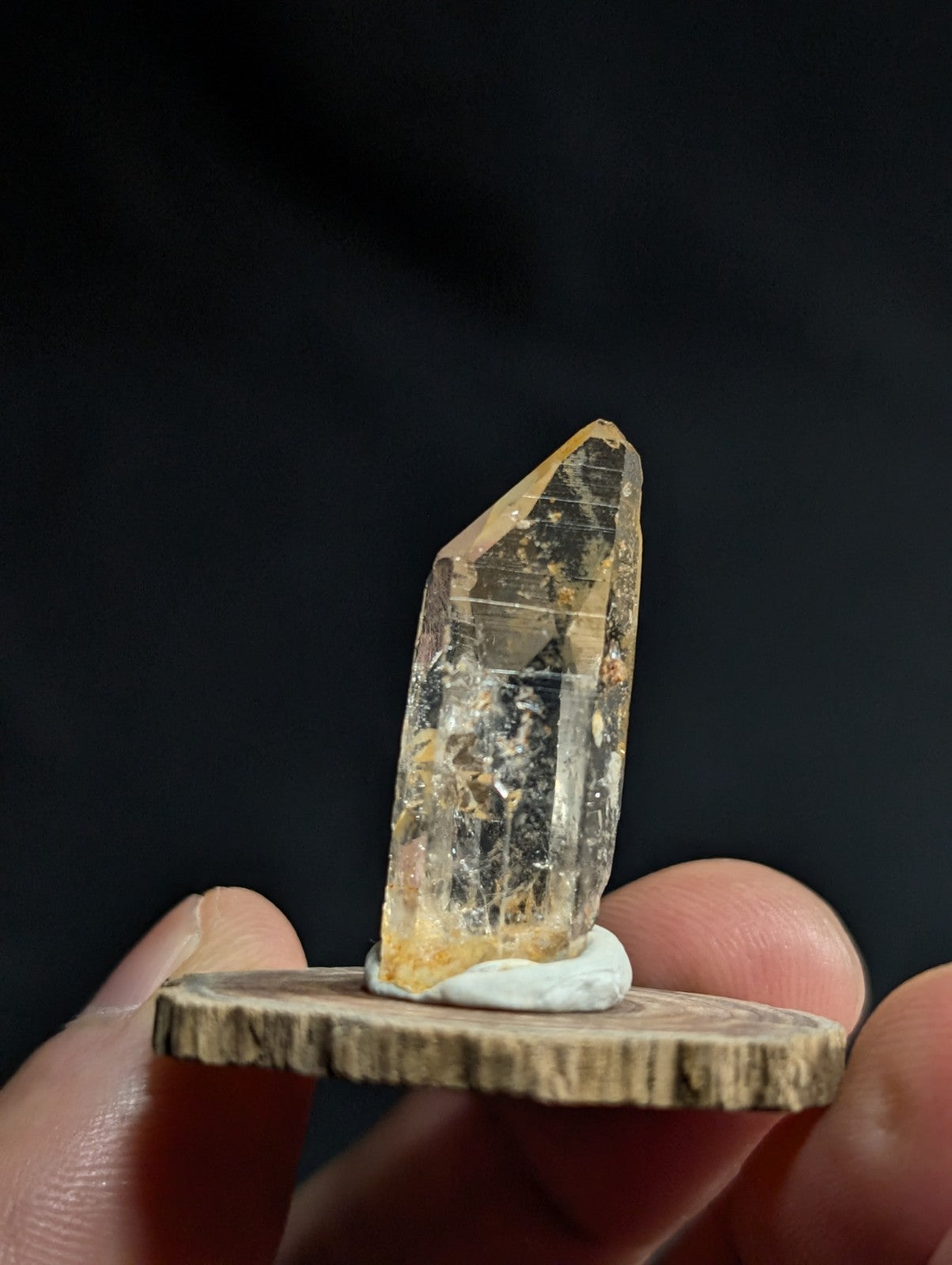 A translucent yellowish quartz crystal with visible internal inclusions, mounted on a rustic wooden base.