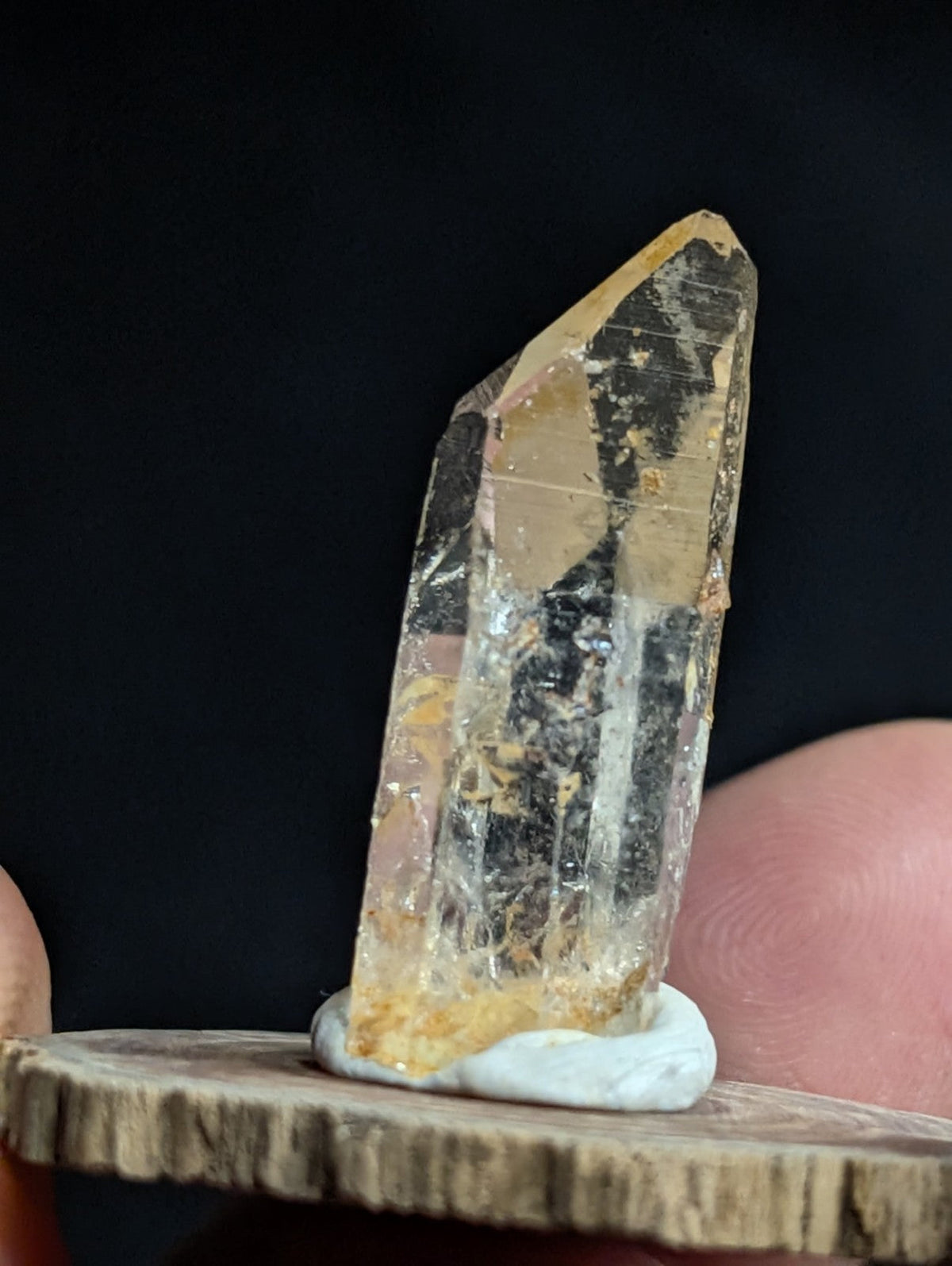 A translucent yellowish quartz crystal with natural inclusions and a pointed tip, displayed on a rustic wooden base.