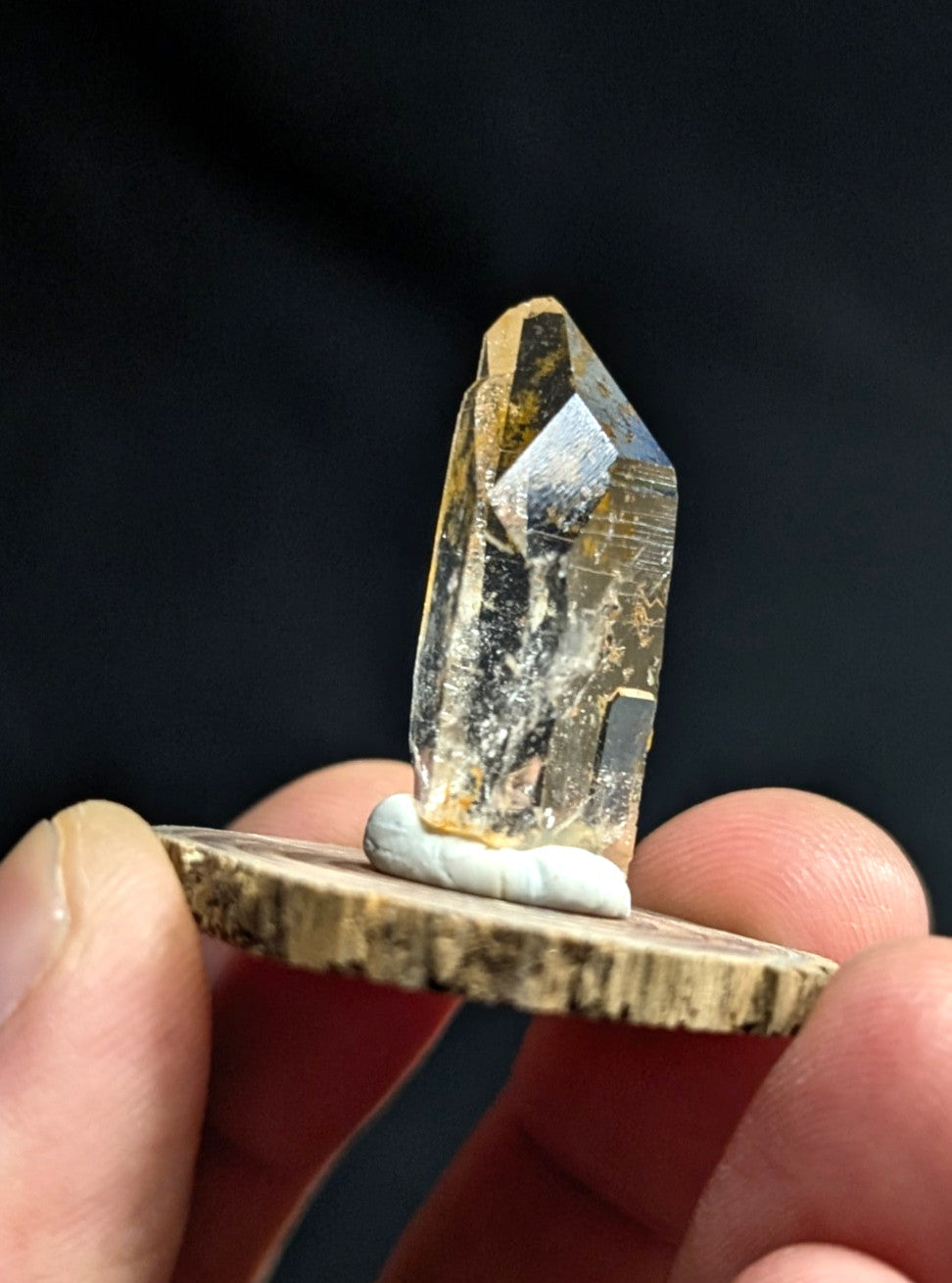 A translucent golden-yellow crystal with a pointed, faceted top and natural inclusions is mounted on a rustic wooden base.