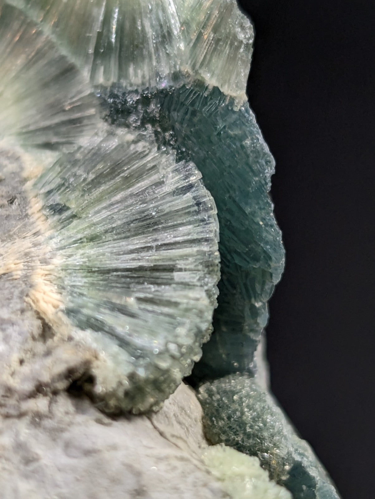 A translucent green mineral specimen featuring radiating, fan-like crystal formations with a rough-textured matrix base.