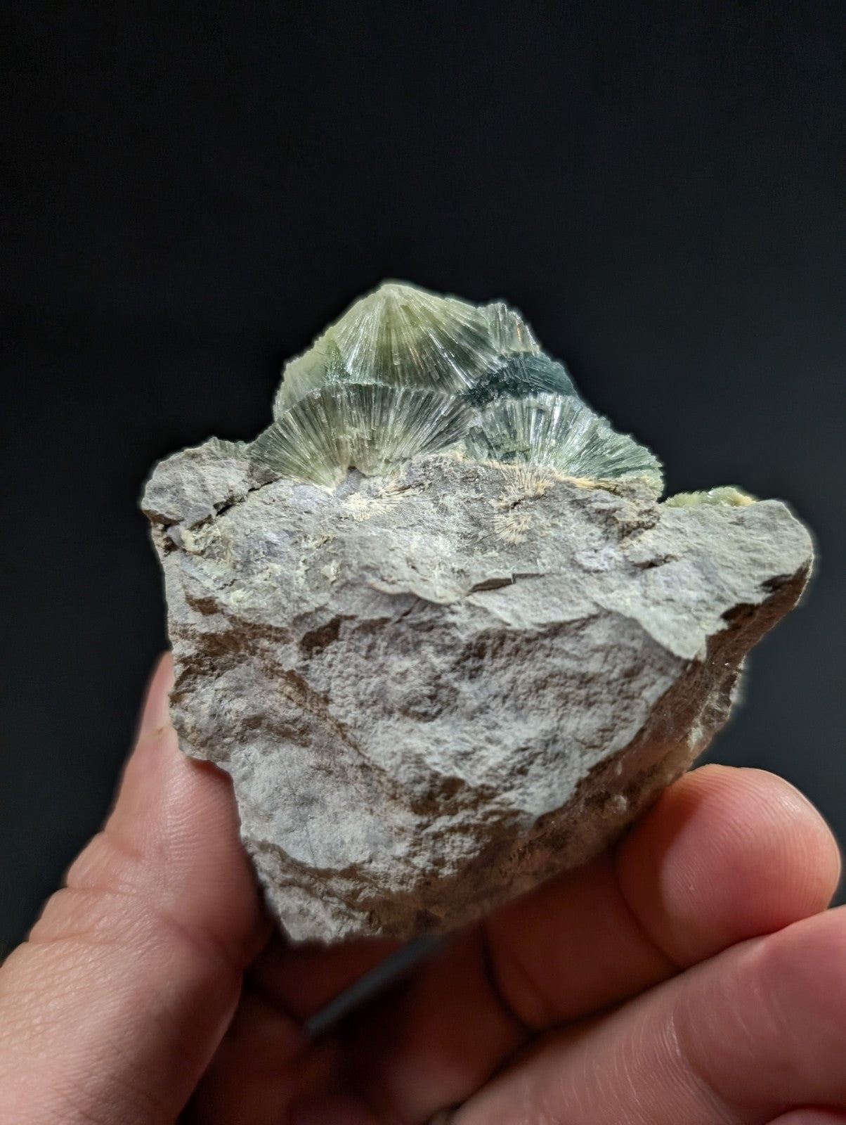 A hand holds a rough, gray rock with a striking greenish-blue crystalline formation on top.
