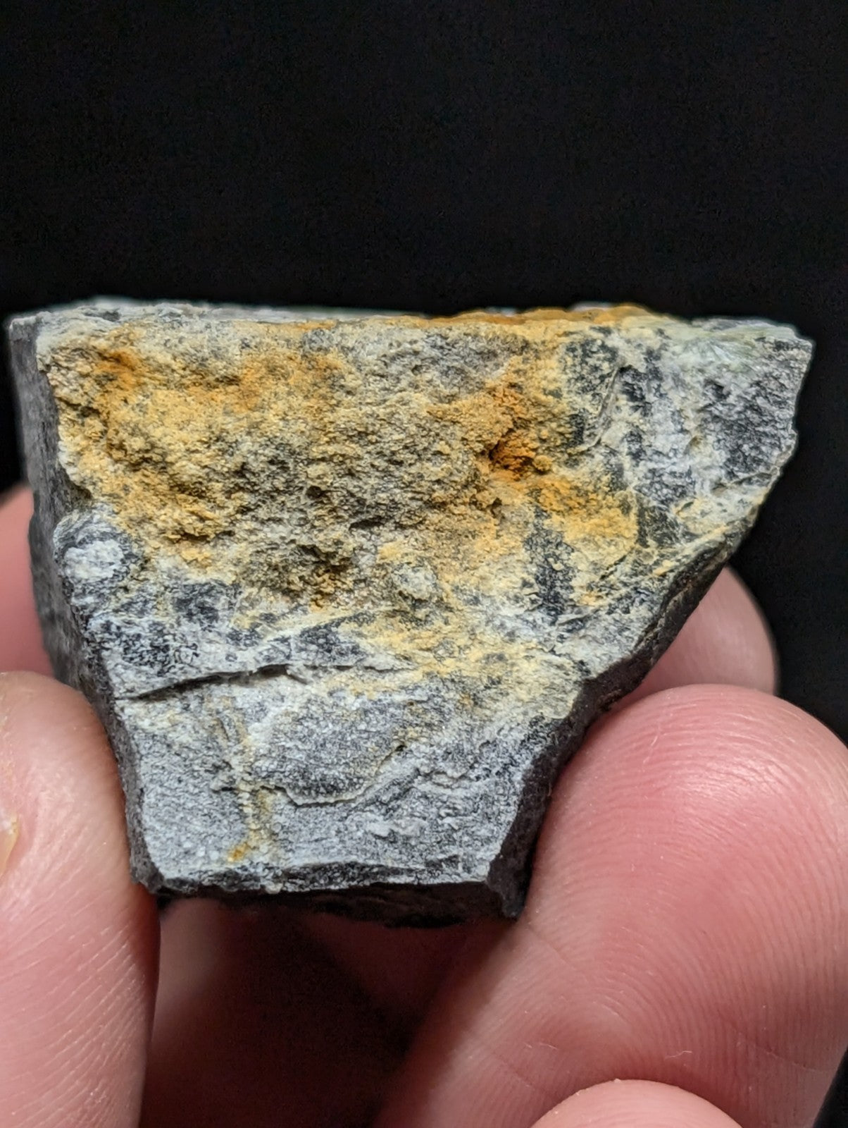 A rugged, irregularly shaped rock fragment with a gray base and patches of vibrant yellow-orange mineral streaks.