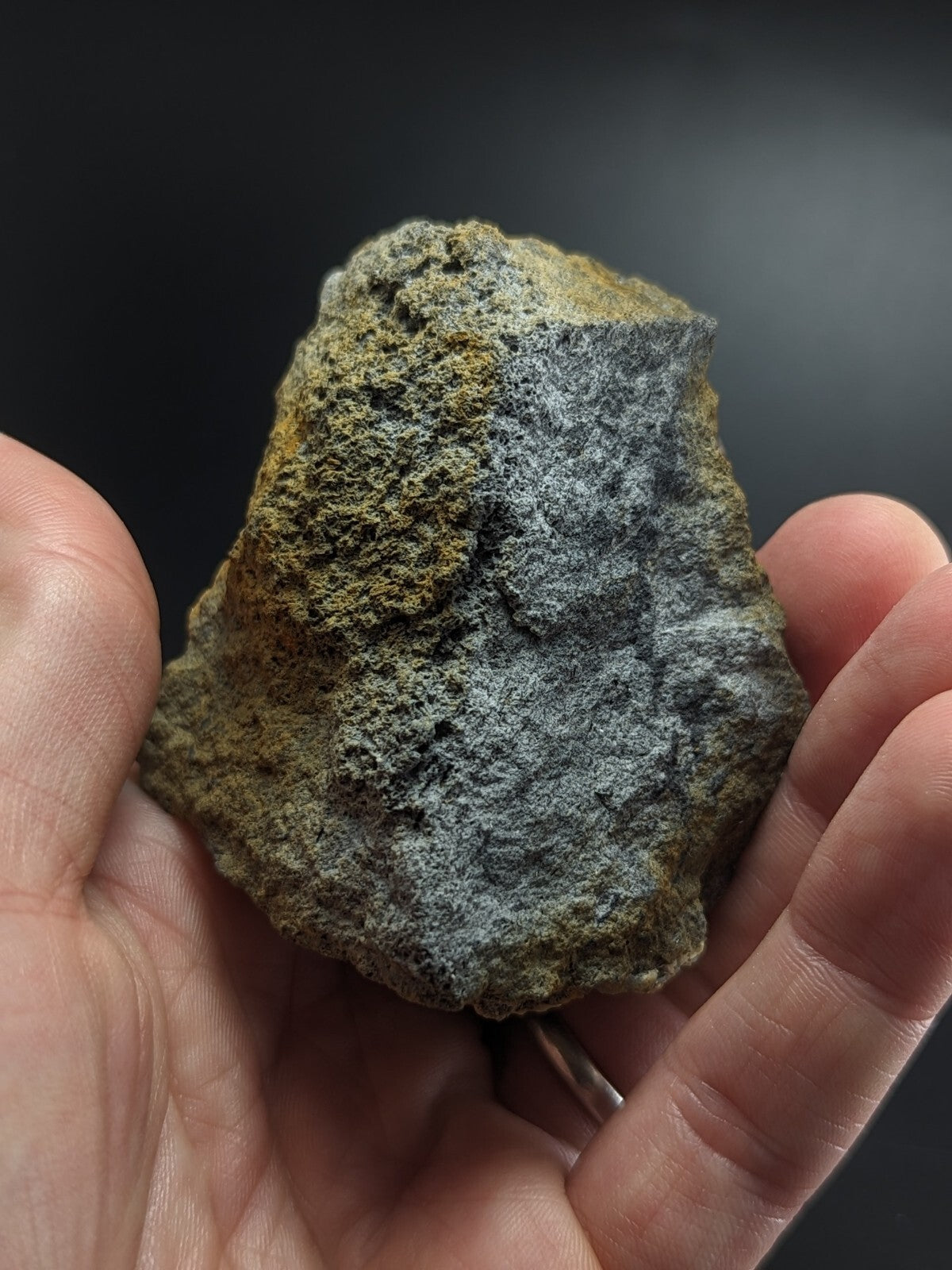A rugged, naturally weathered rock with a textured surface featuring patches of gray and earthy yellow-brown hues.