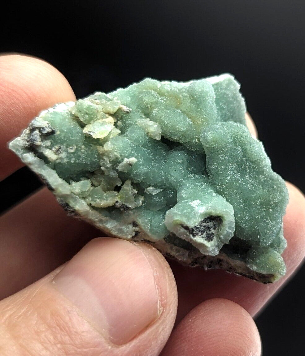 A hand holds a textured, light green mineral specimen with crystalline formations and darker patches.