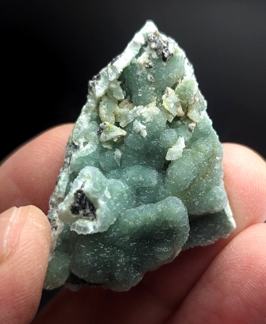 A triangular, translucent green mineral specimen with a crystalline texture and white matrix.