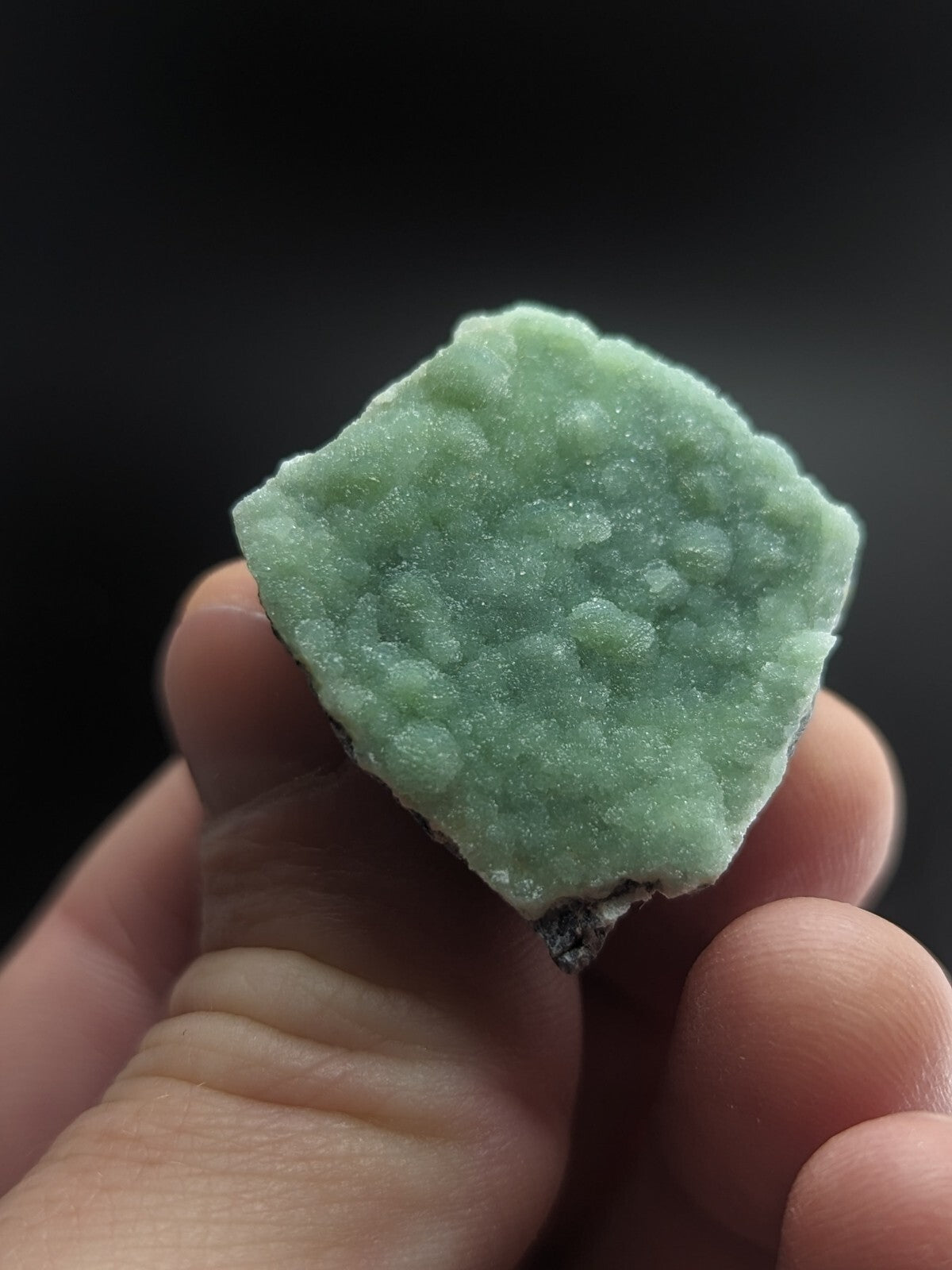 A pale green, textured mineral specimen with a crystalline surface held in hand.