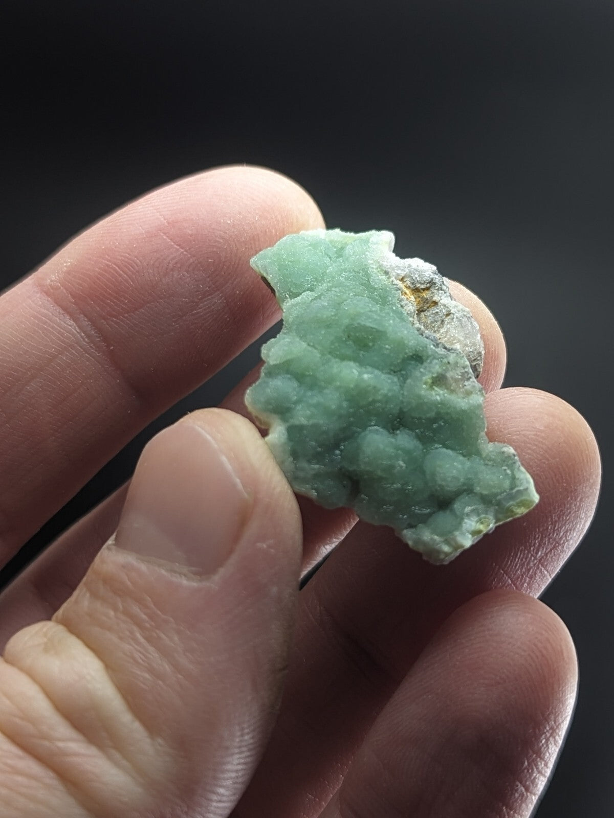 A translucent light green mineral specimen with a textured, clustered surface and some white crystalline areas.