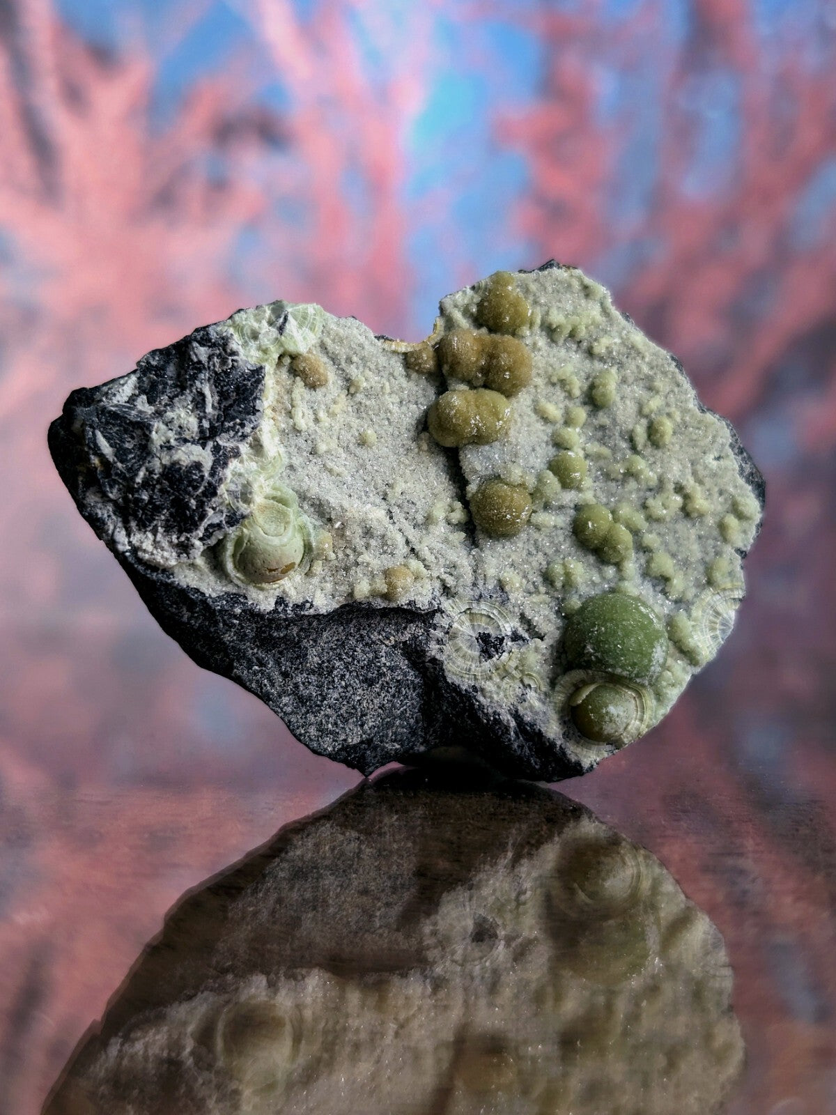 A striking green and black mineral specimen featuring rounded, glossy nodules embedded in a textured matrix.