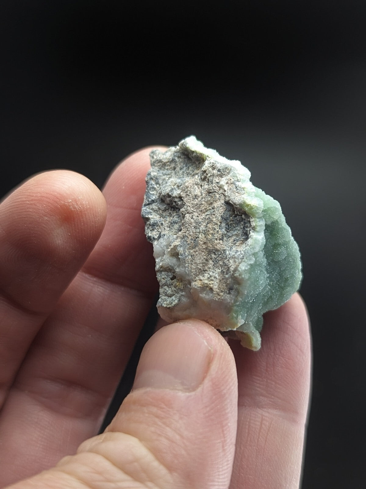 A rough, pale green jade specimen with a textured surface and visible mineral matrix.