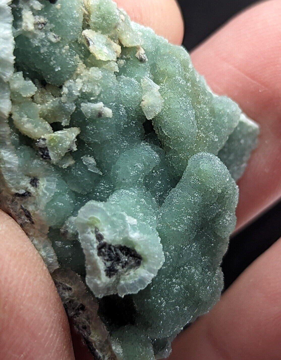 A translucent green mineral specimen with a crystalline, textured surface and dark inclusions.