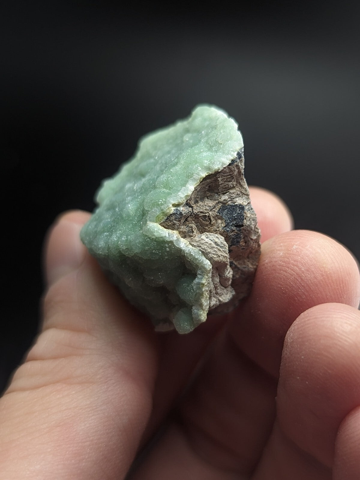 A rough, pale green mineral specimen with a crystalline texture and earthy brown matrix.