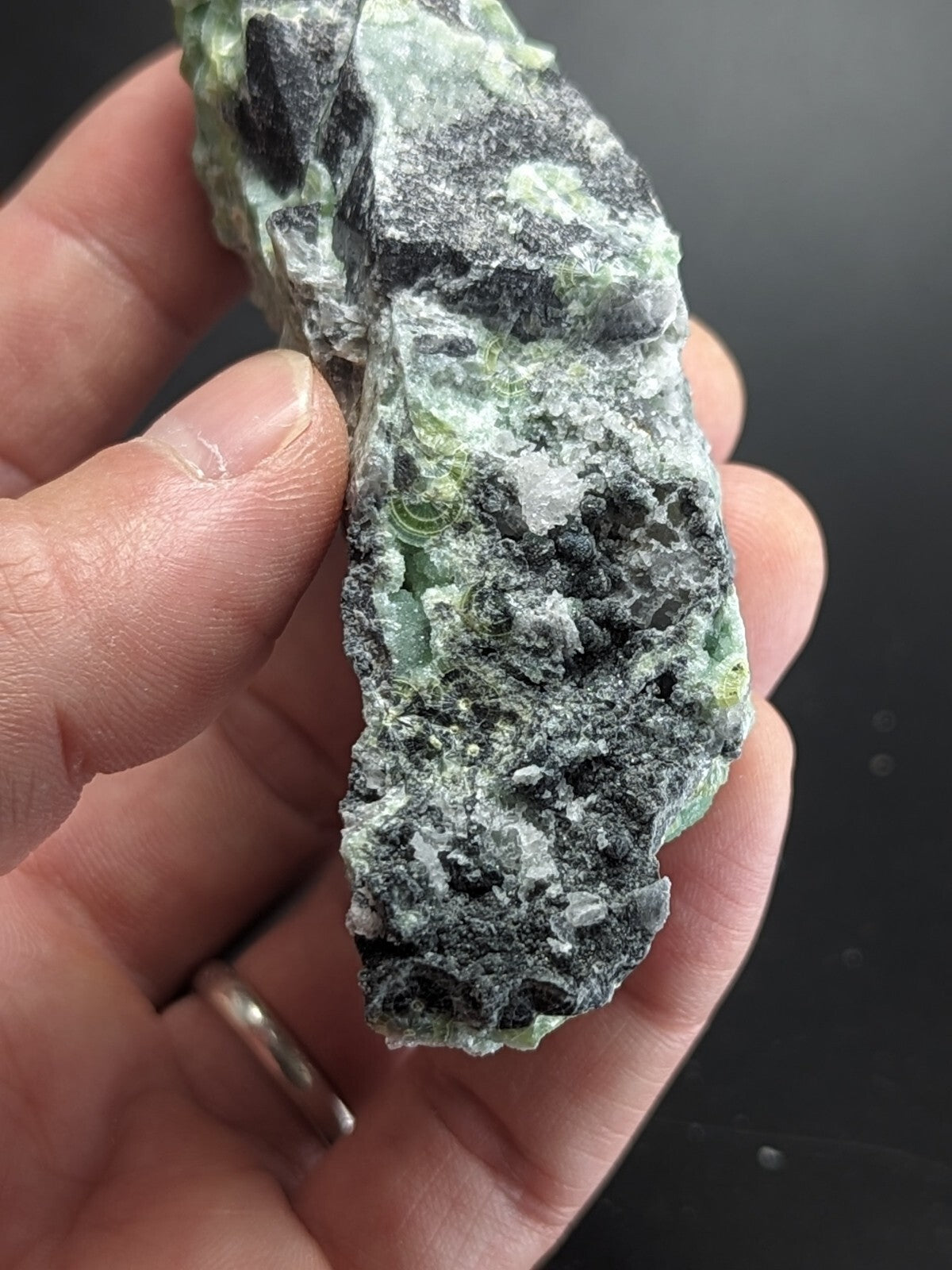 A rough, irregularly shaped piece of green and black mineral with a textured surface.