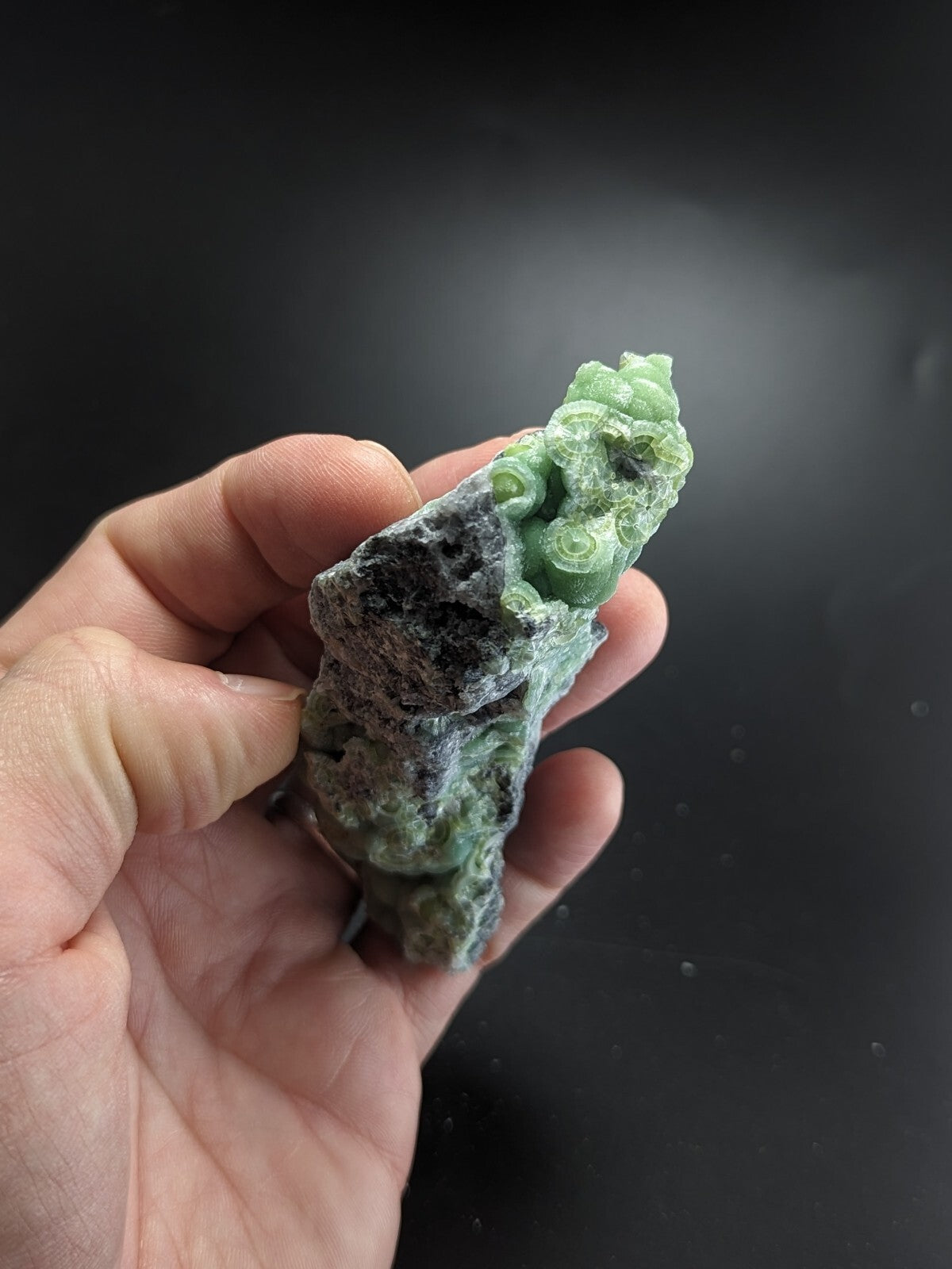 A hand holds a green, carved jade figurine with intricate spiral patterns and a rough-textured base.