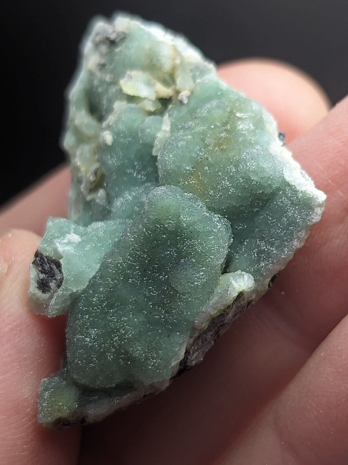 A translucent light green mineral specimen with a crystalline, rough-textured surface and patches of white and dark matrix.