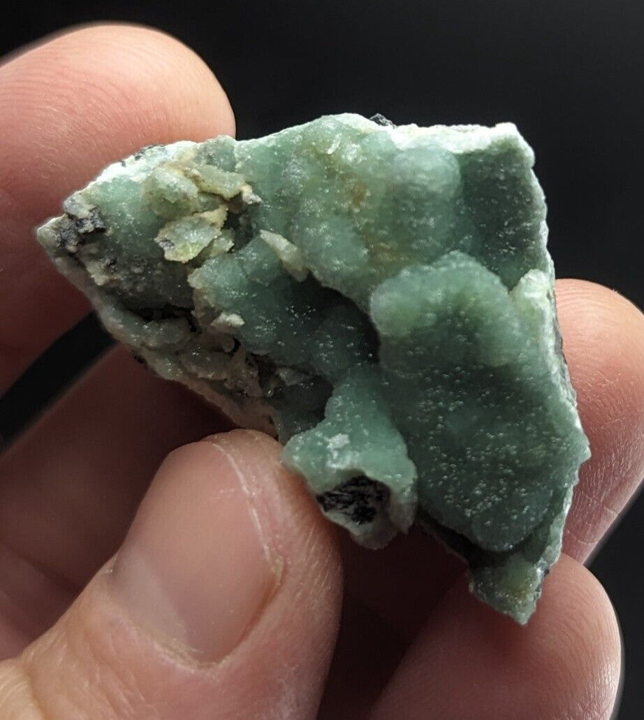 A rough, pale green mineral specimen with a crystalline texture and patches of darker matrix.