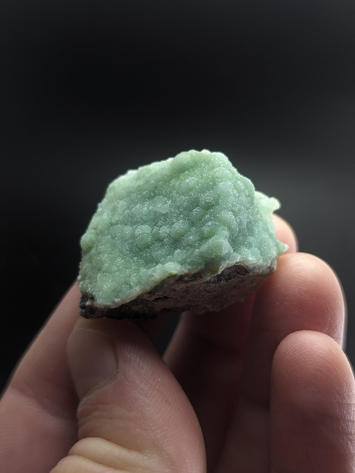 A pale green, textured mineral specimen with a rough, crystalline surface and dark base.