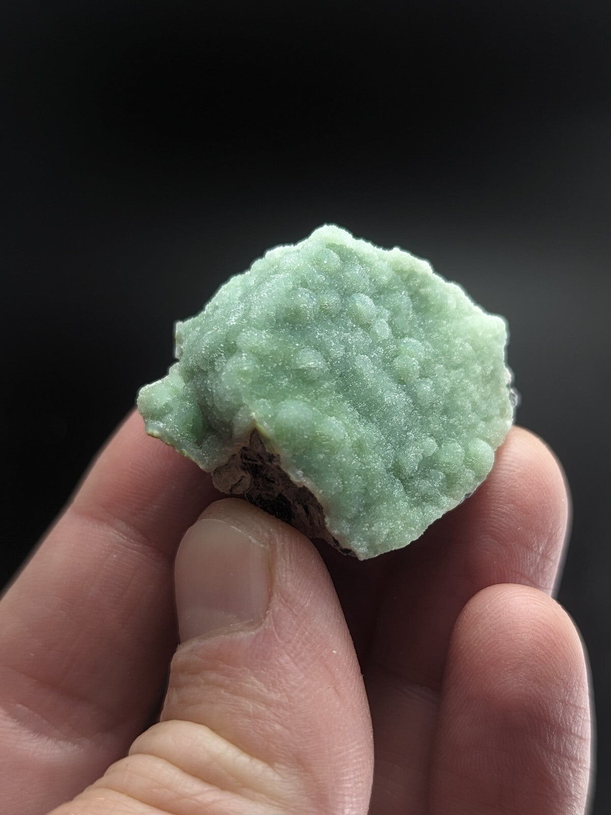 A pale green, textured mineral specimen with a rough, bumpy surface held in someone’s hand.
