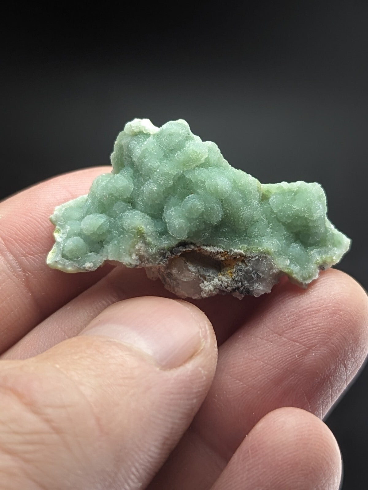 A pale green, textured mineral specimen with a clustered, bumpy surface and some darker earthy patches at its base.