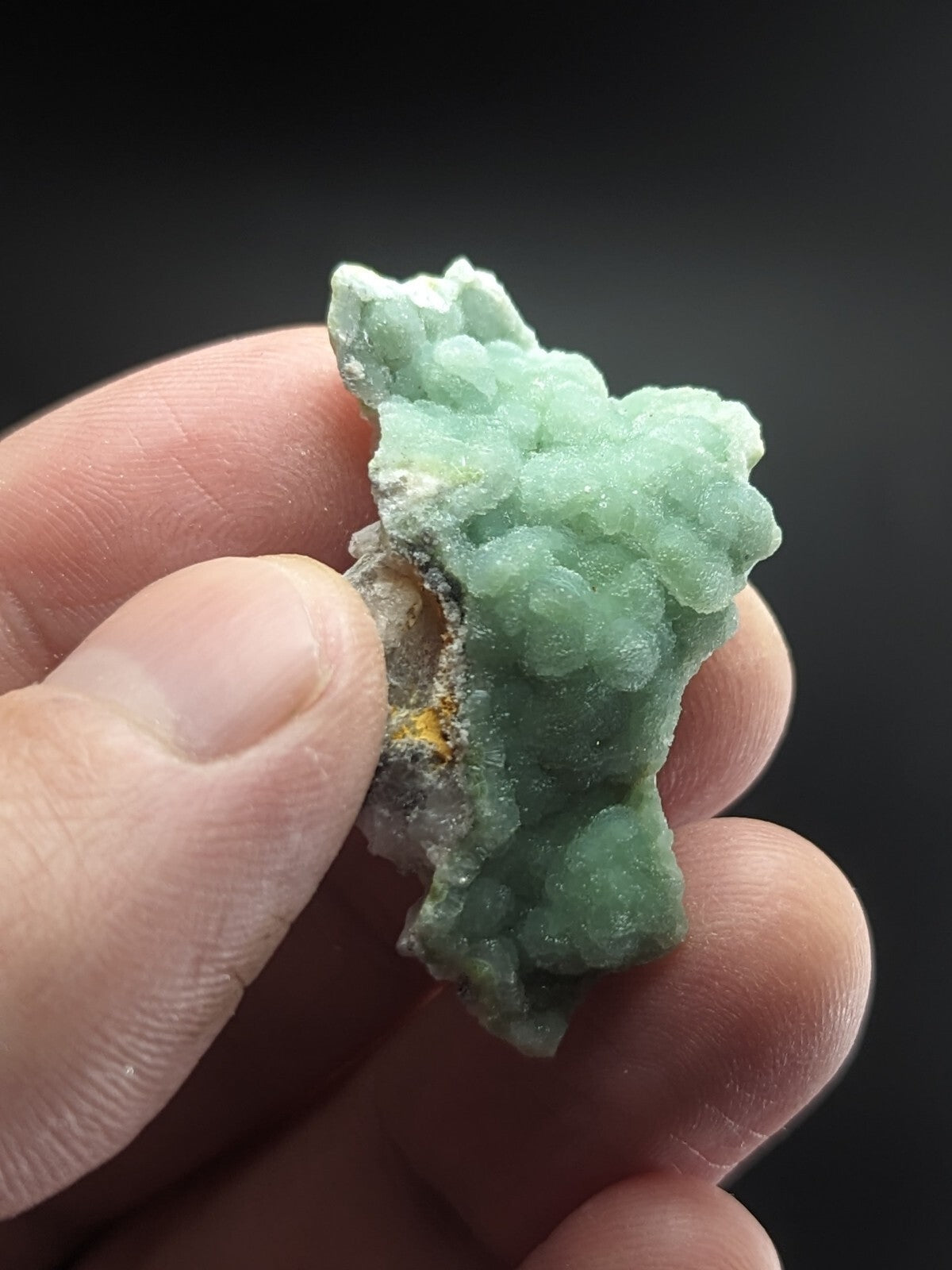 A pale green, crystalline mineral specimen with a rough, textured surface and some white matrix material.