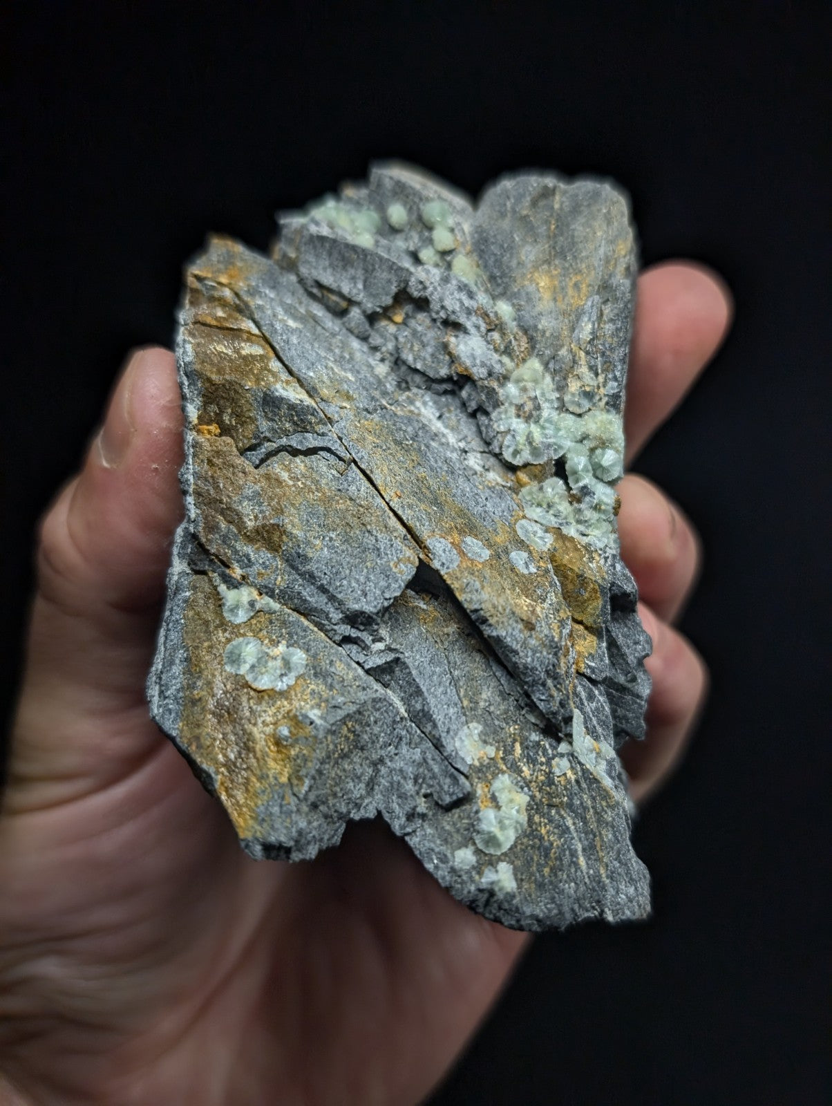 A rugged, irregularly shaped mineral specimen with a gray base accented by patches of yellow and light green crystalline formations.